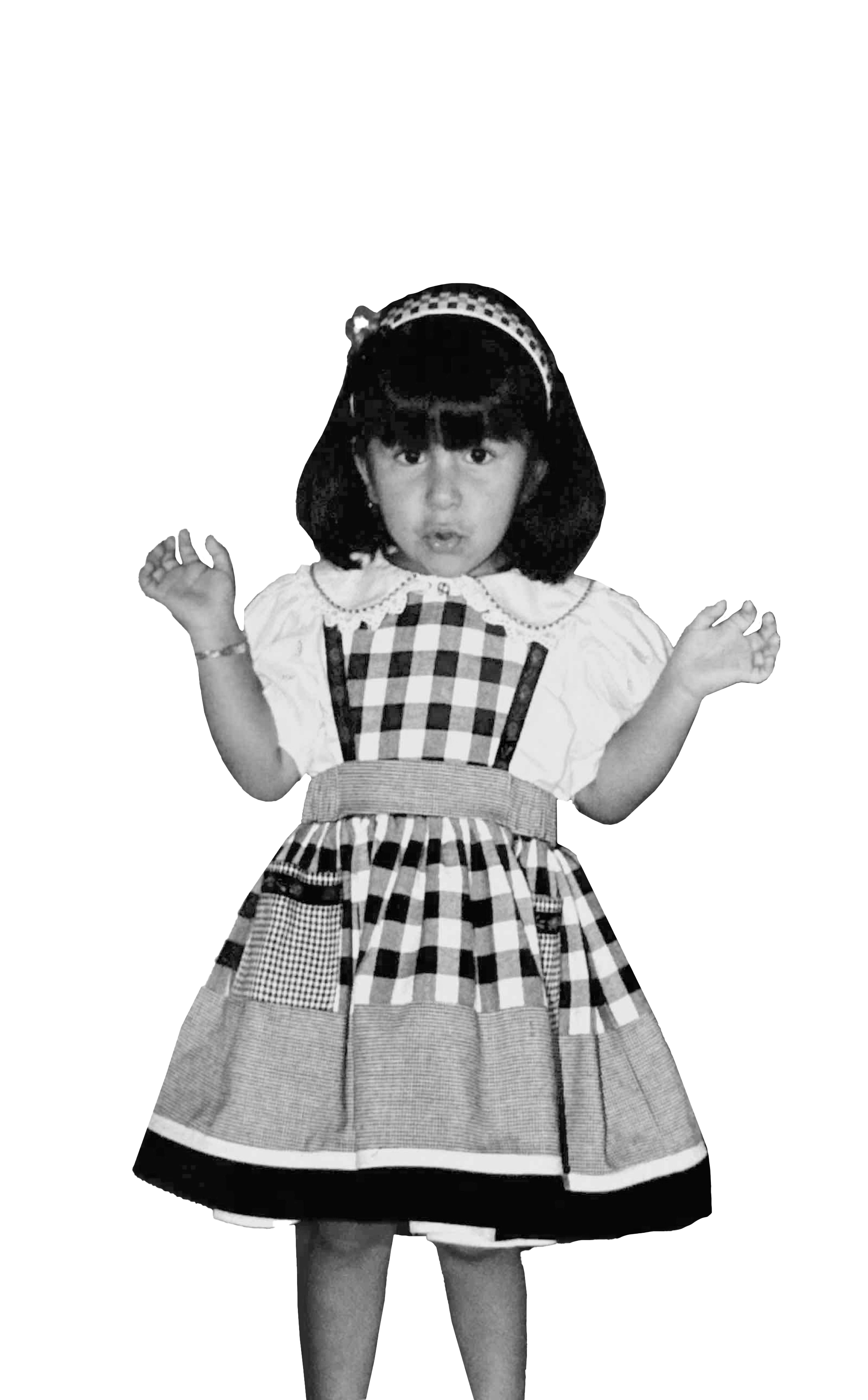 A young girl wearing a checkered dress with a bow in her hair and her hands raised, standing against a background of black and white.