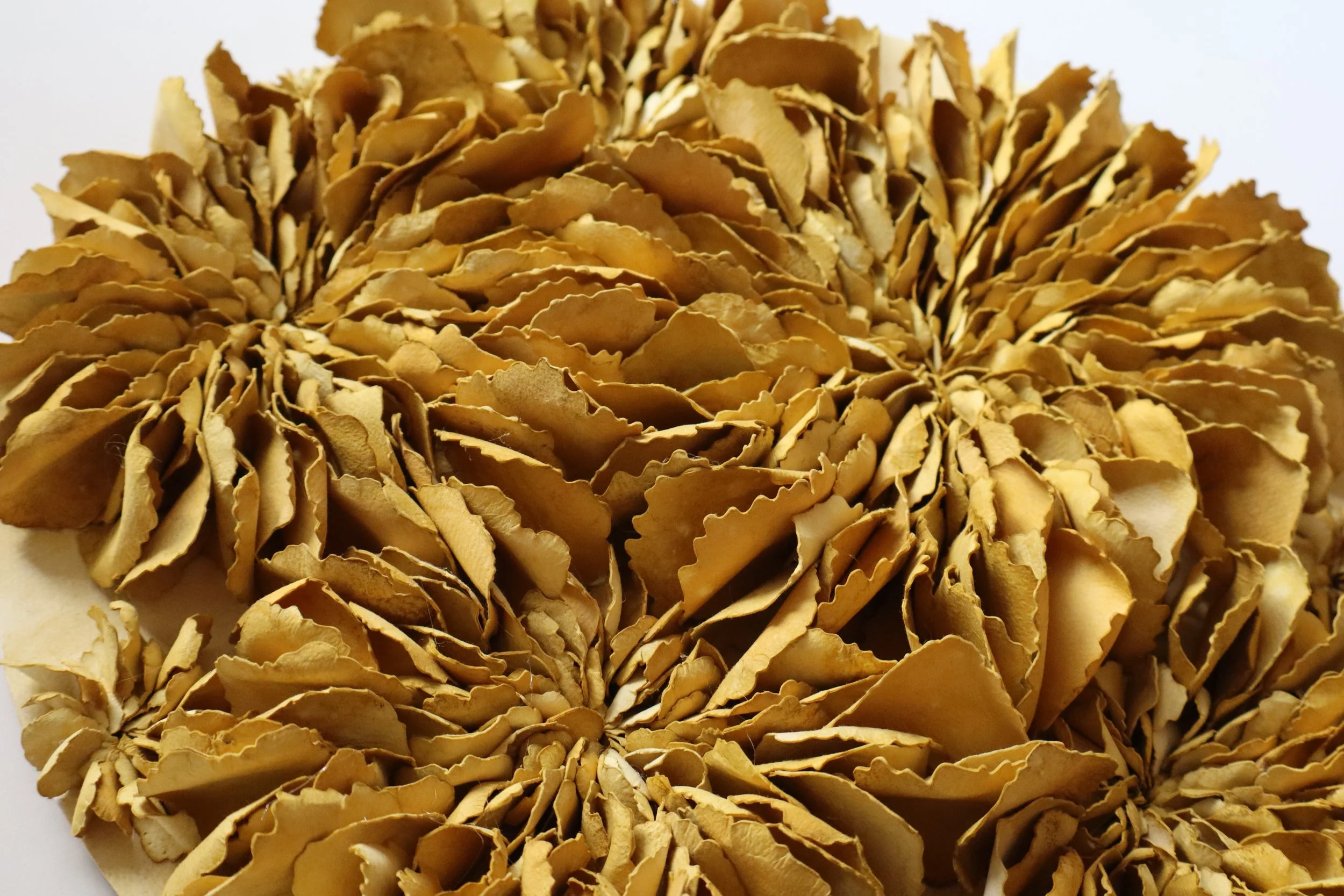 Close-up of a large decorative object made of thin, curled, tan-colored paper or material resembling wood shavings, arranged in a spherical shape.