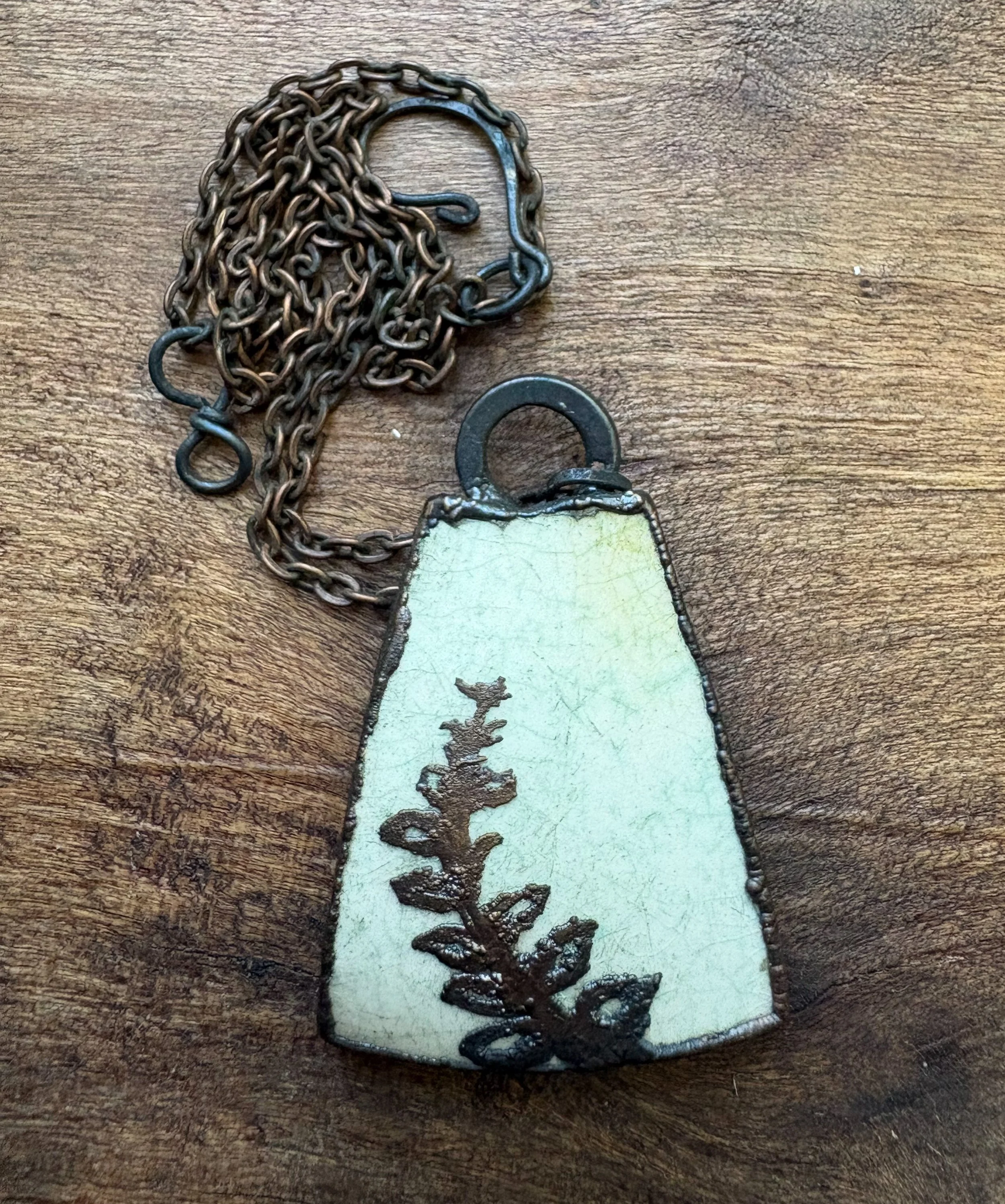 A metal chain shaped like a dog's head and a fourth of the body on a wooden surface. There is also a metal tag with a rough surface and symbols or characters on it.