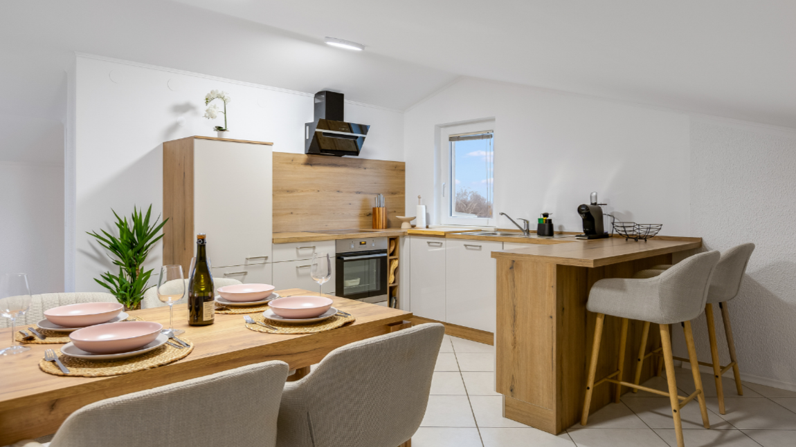 Modern kitchen and dining area with wooden accents, white cabinetry, and a table set with pink plates, glasses, and cutlery.