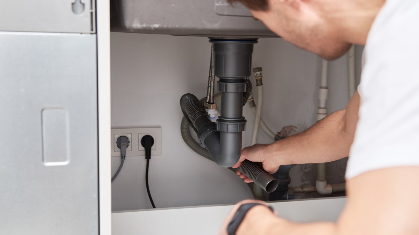 Person repairing plumbing under a kitchen sink.