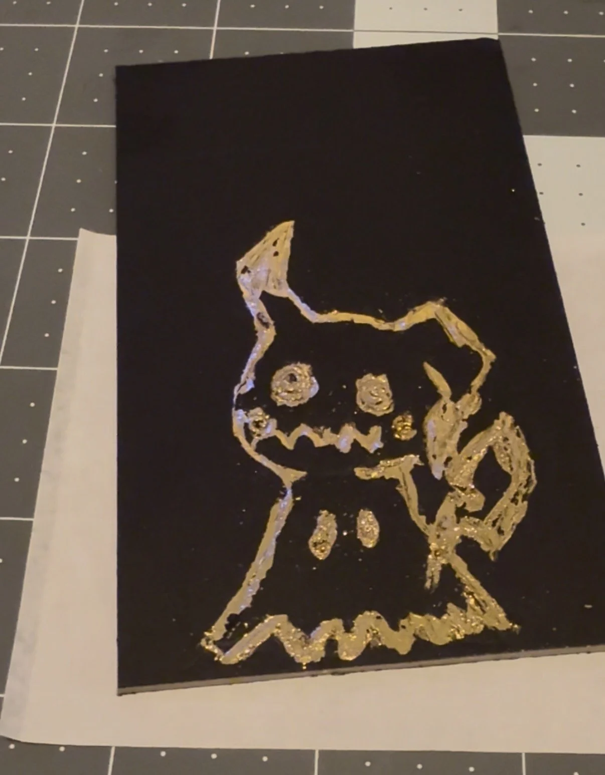 Black card with a gold glitter drawing of a witch's hat and a jack-o'-lantern face, Halloween themed.