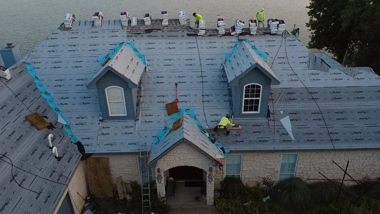 Workers installing shingles on a house roof under construction.