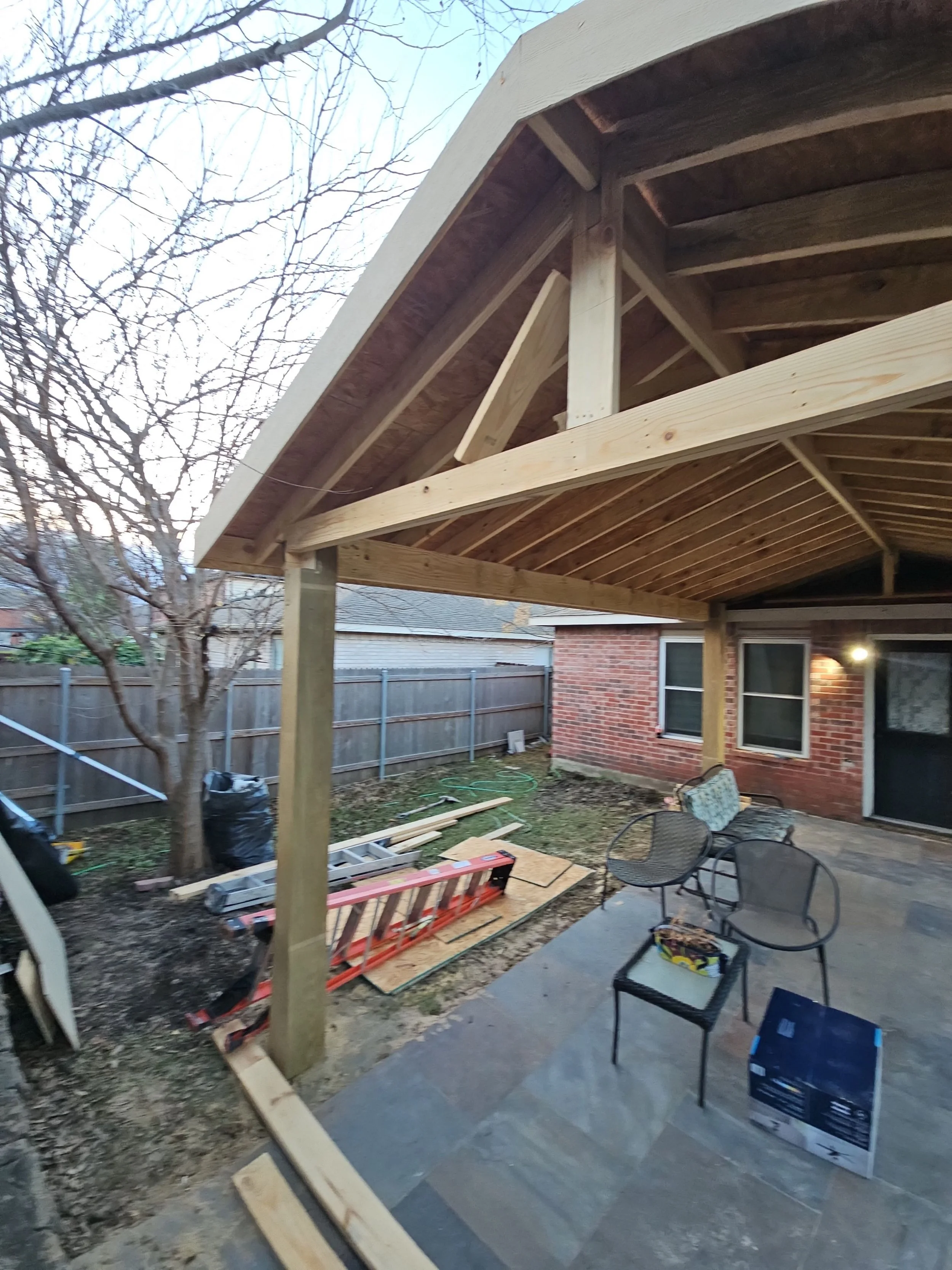 Backyard under construction with wooden framework for a porch or deck, outdoor furniture, and construction tools.