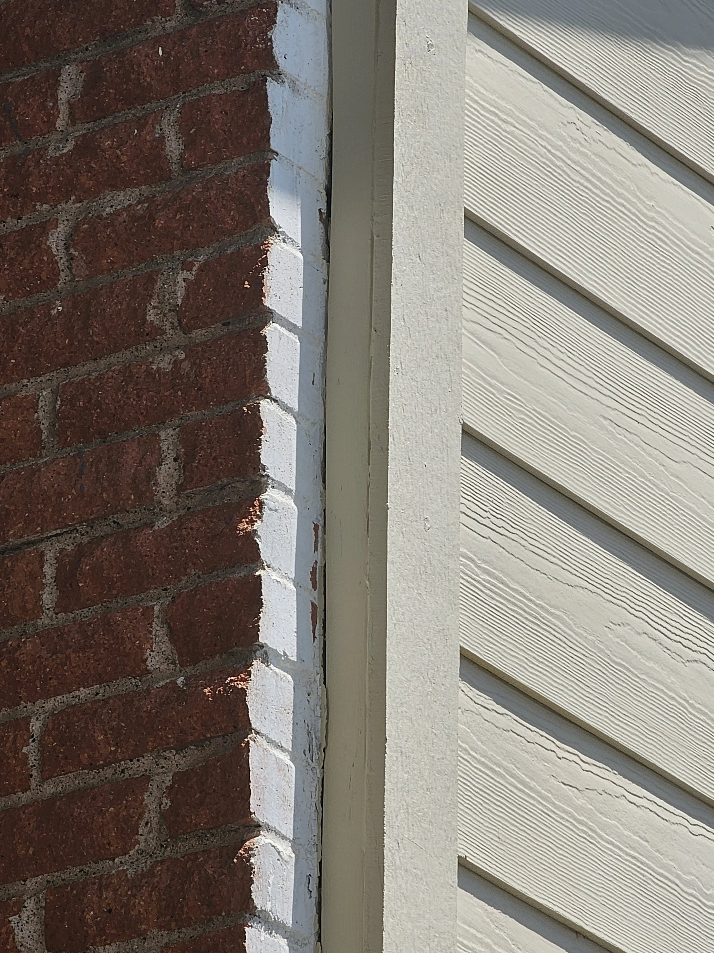 Close-up of a corner where a red brick wall meets a white painted wall and white vinyl siding.