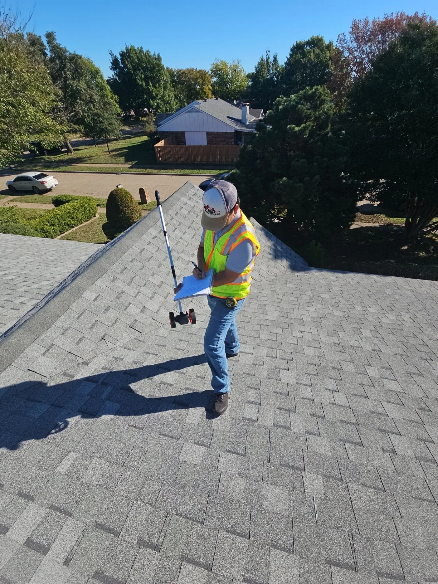 A person standing on a rooftoop taking notes with a clipboard and a measuring tool.