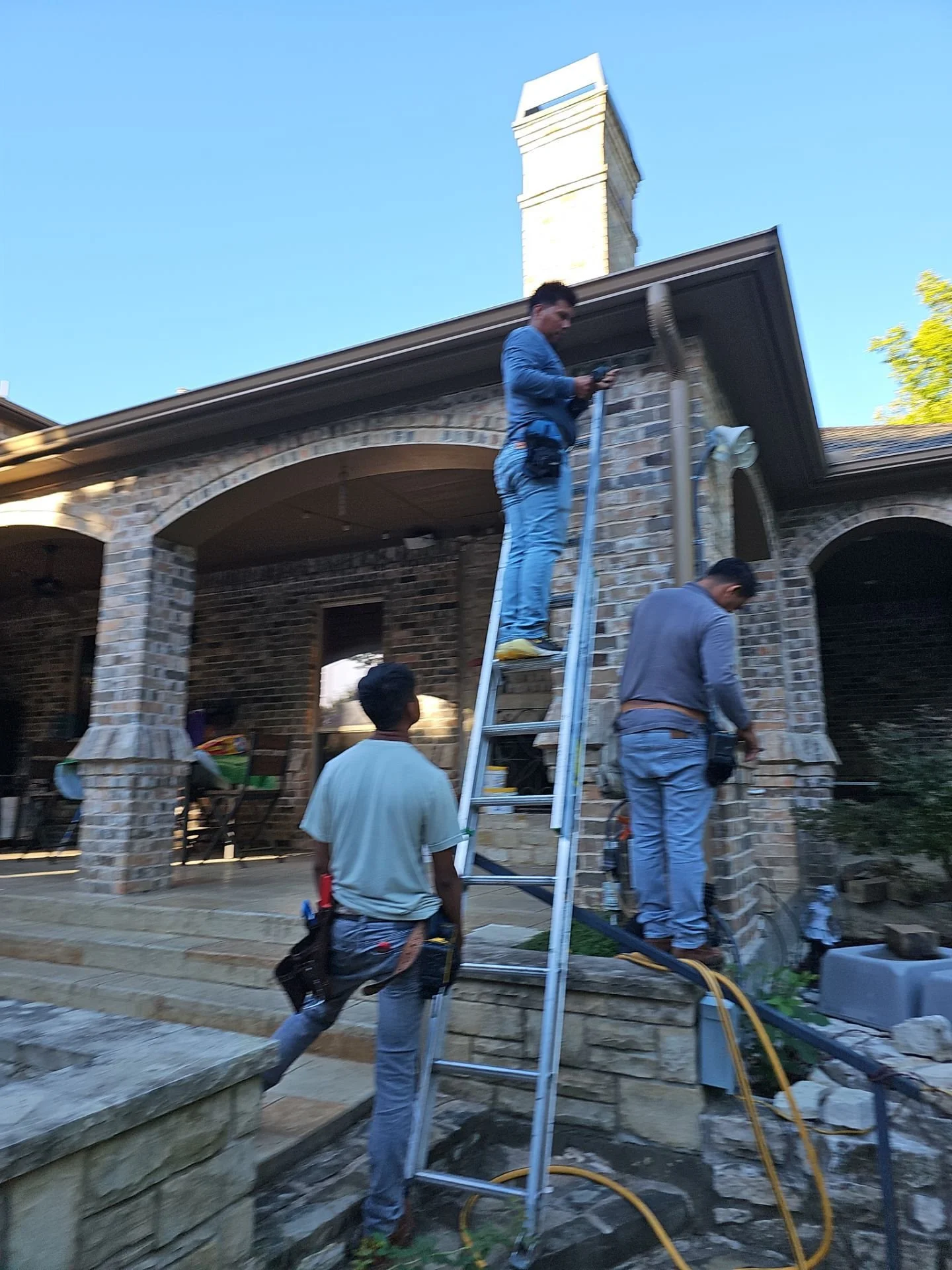 Construction workers installing or repairing a chimney on a brick house with a ladder and tools.