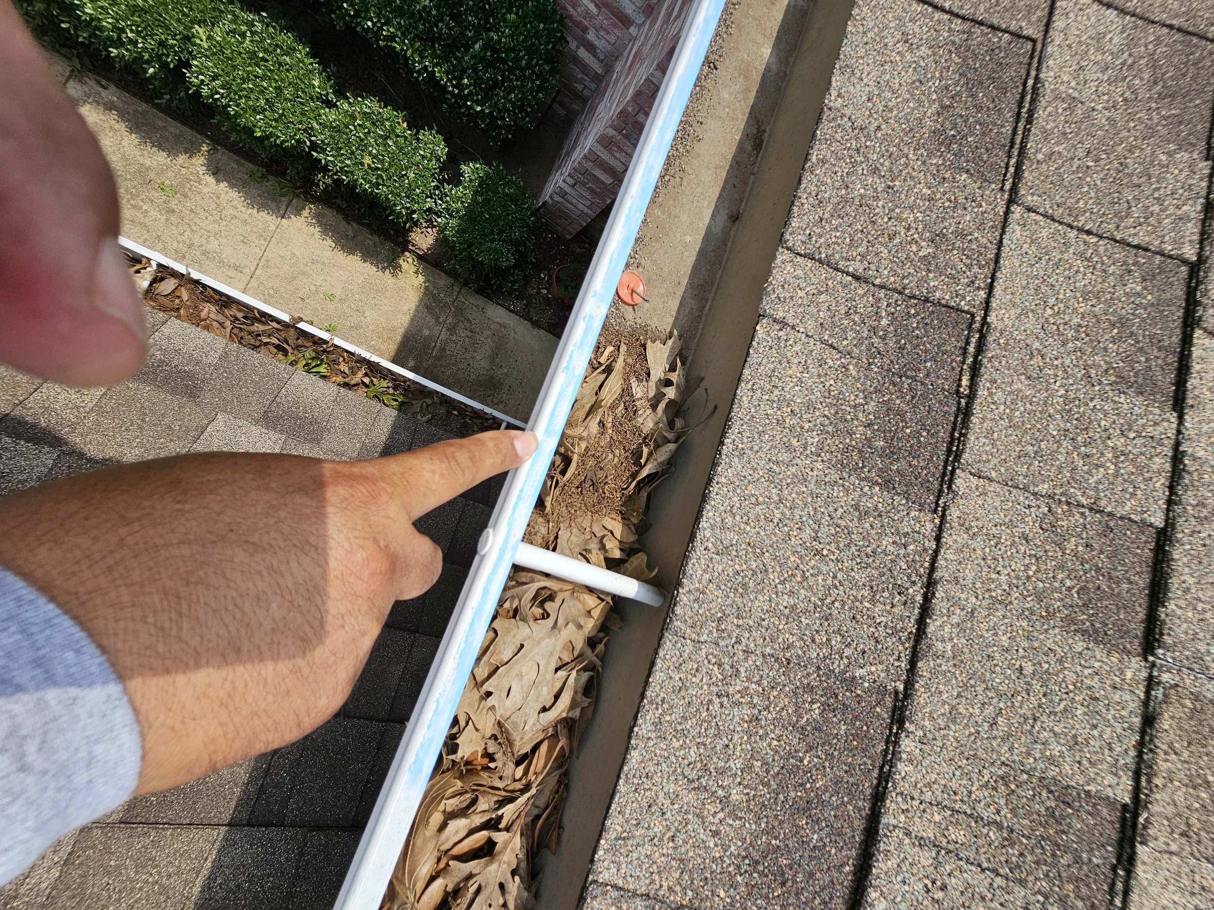 Person installing or inspecting a white metal railing outside on a concrete surface with greenery and leaves nearby.
