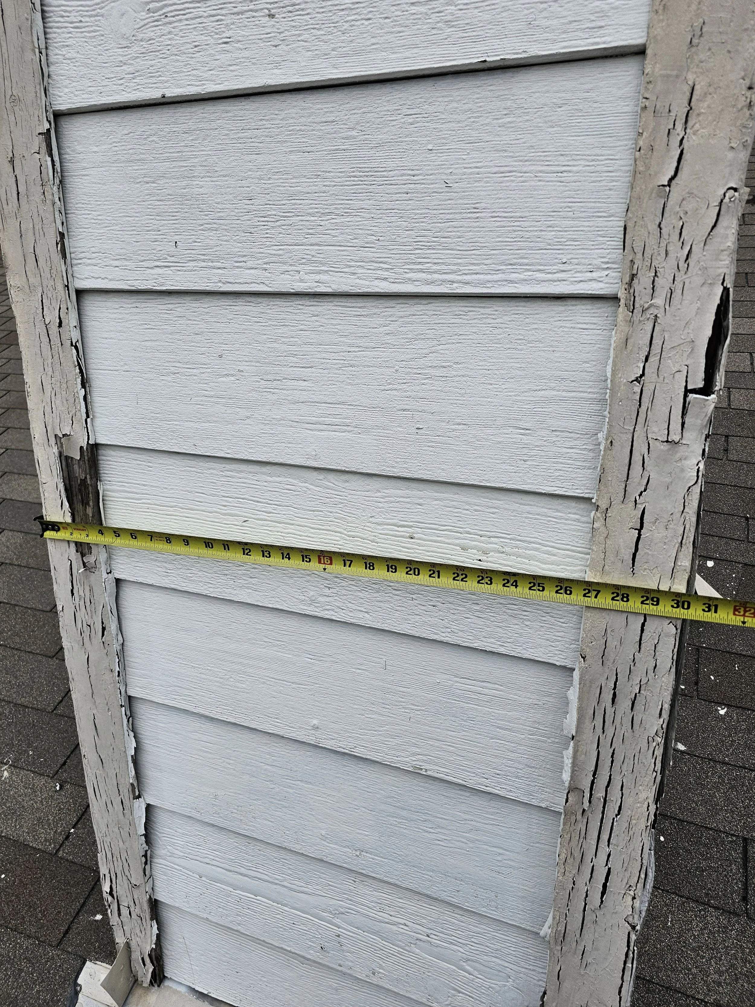 A weathered white wooden wall with peeling paint and a yellow measuring tape stretched across it, showing a measurement of approximately 31 inches.