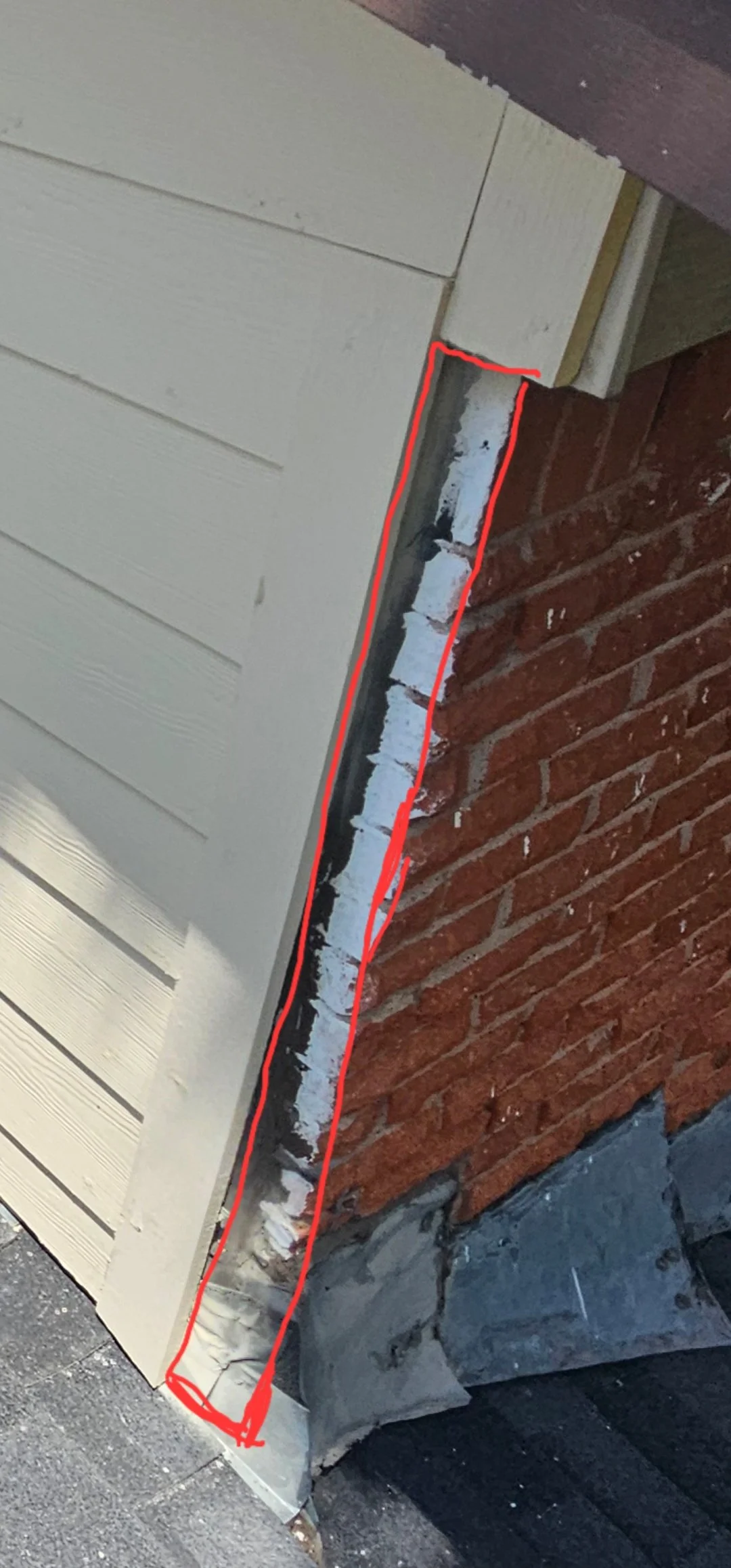 Close-up of a building corner with brick wall, siding, and trim, highlighting an area marked with a red line indicating potential repair or inspection zone.