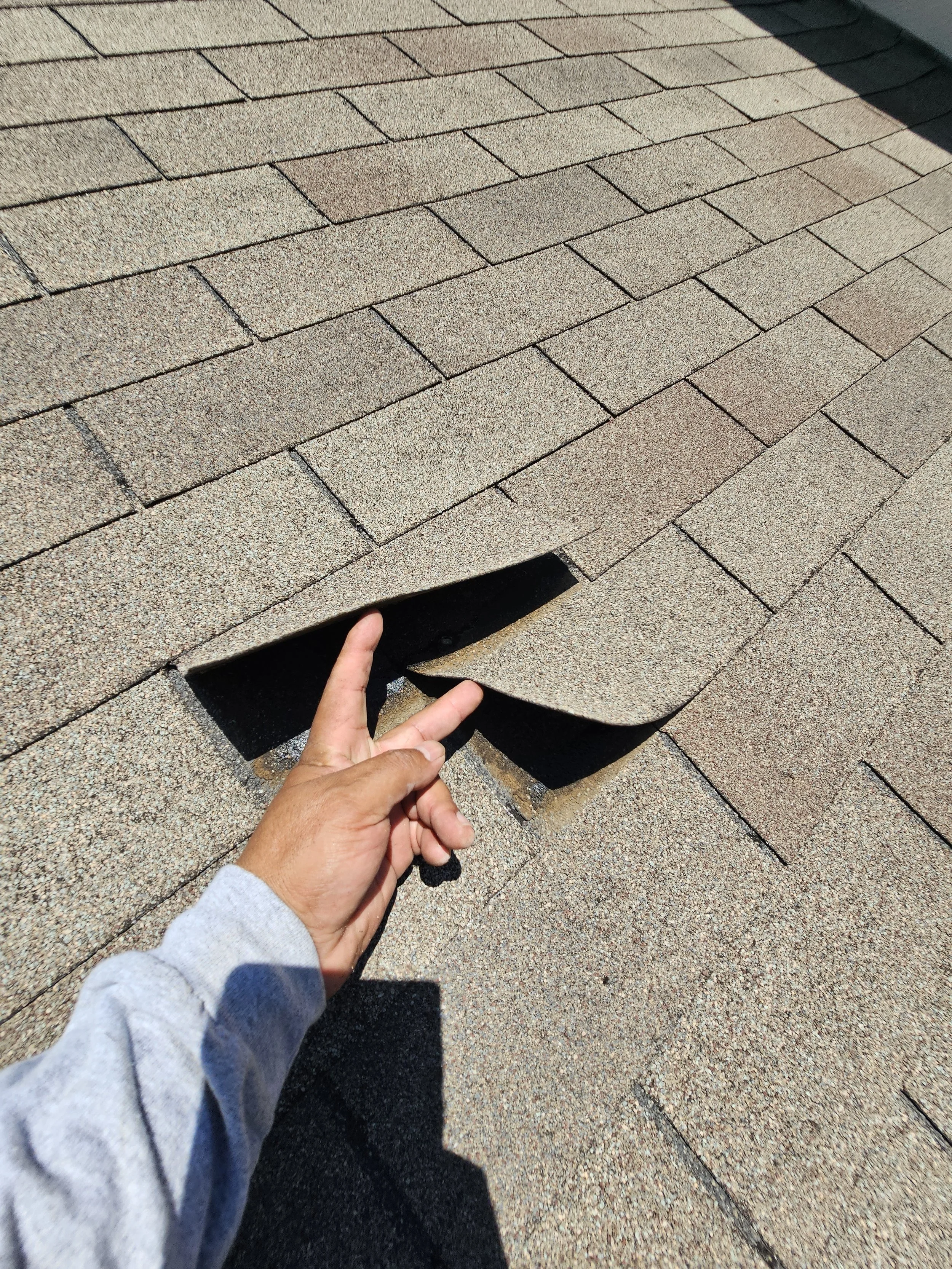 A person pulling back asphalt roofing shingles to reveal the layer underneath.