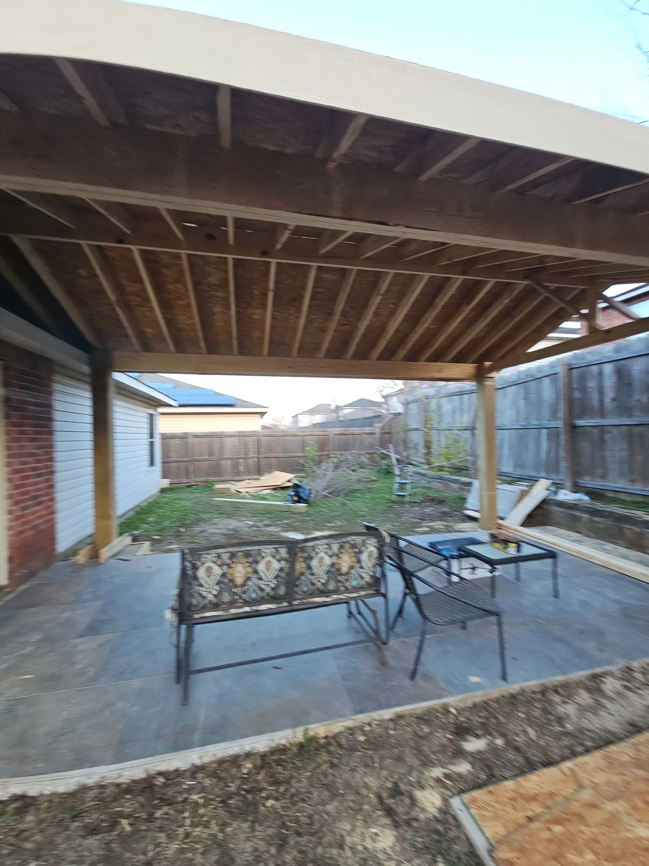 Backyard patio area with a covered wooden ceiling, metal framed patio furniture, and a wooden fence in the background.