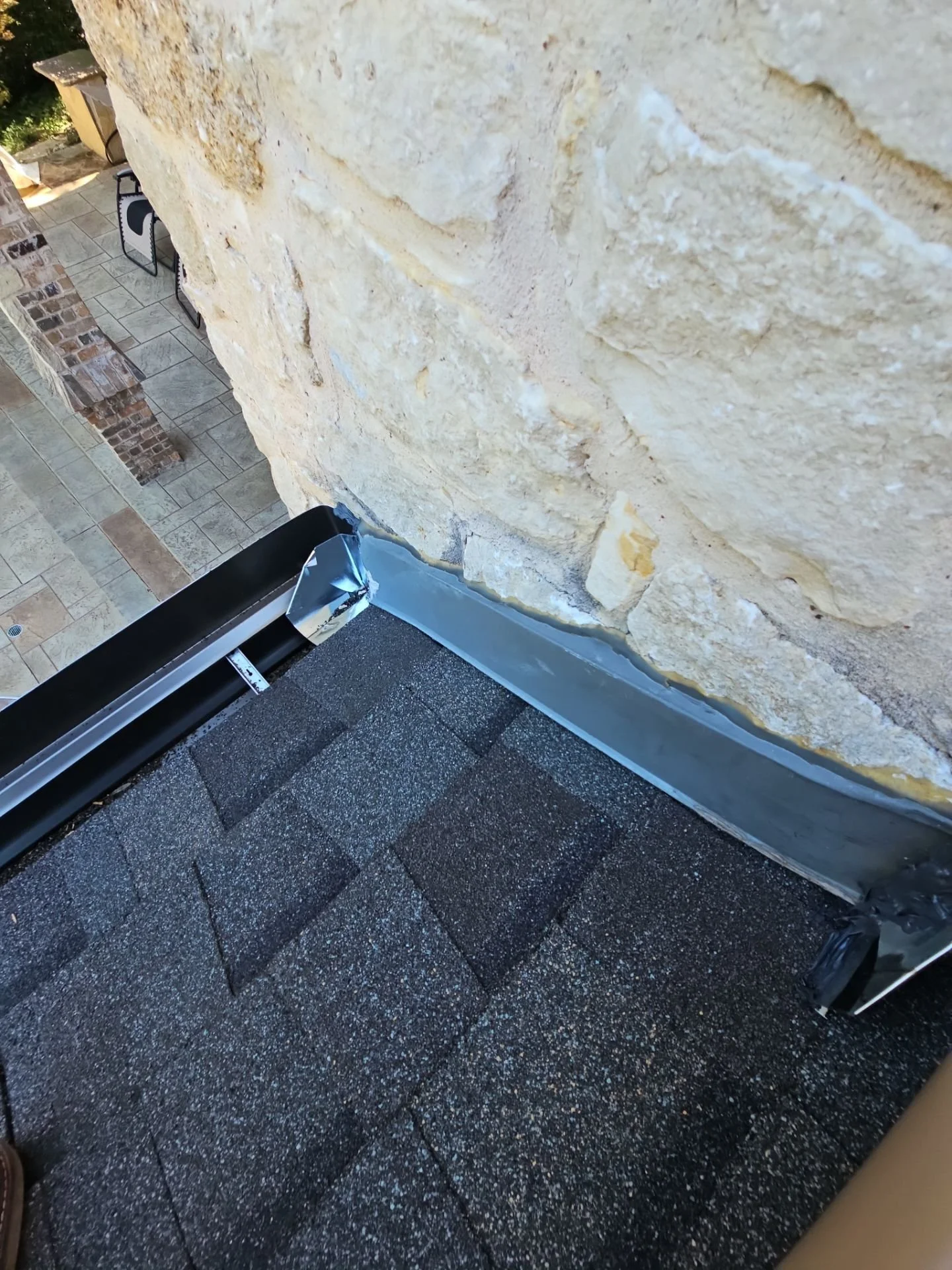 Close-up of a beige brick wall and a section of a porch with dark gray tiles and a black gutter at the bottom.