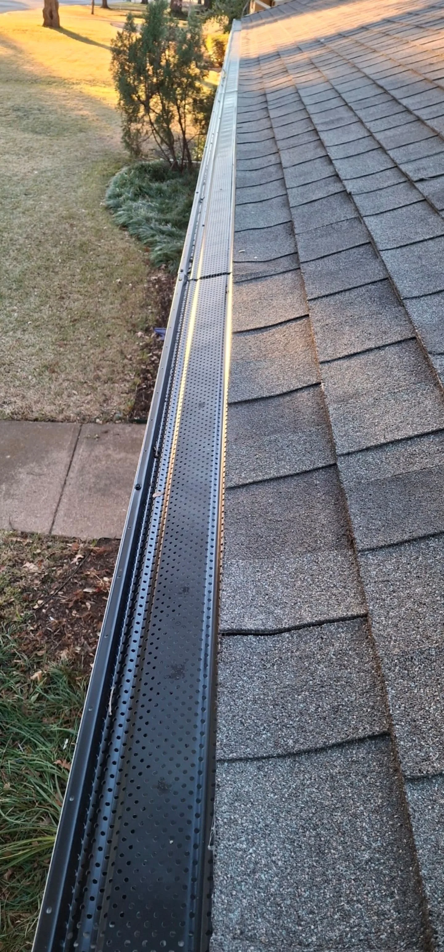 Close-up of a house roof with asphalt shingles and a metal gutter system installed along the edge.