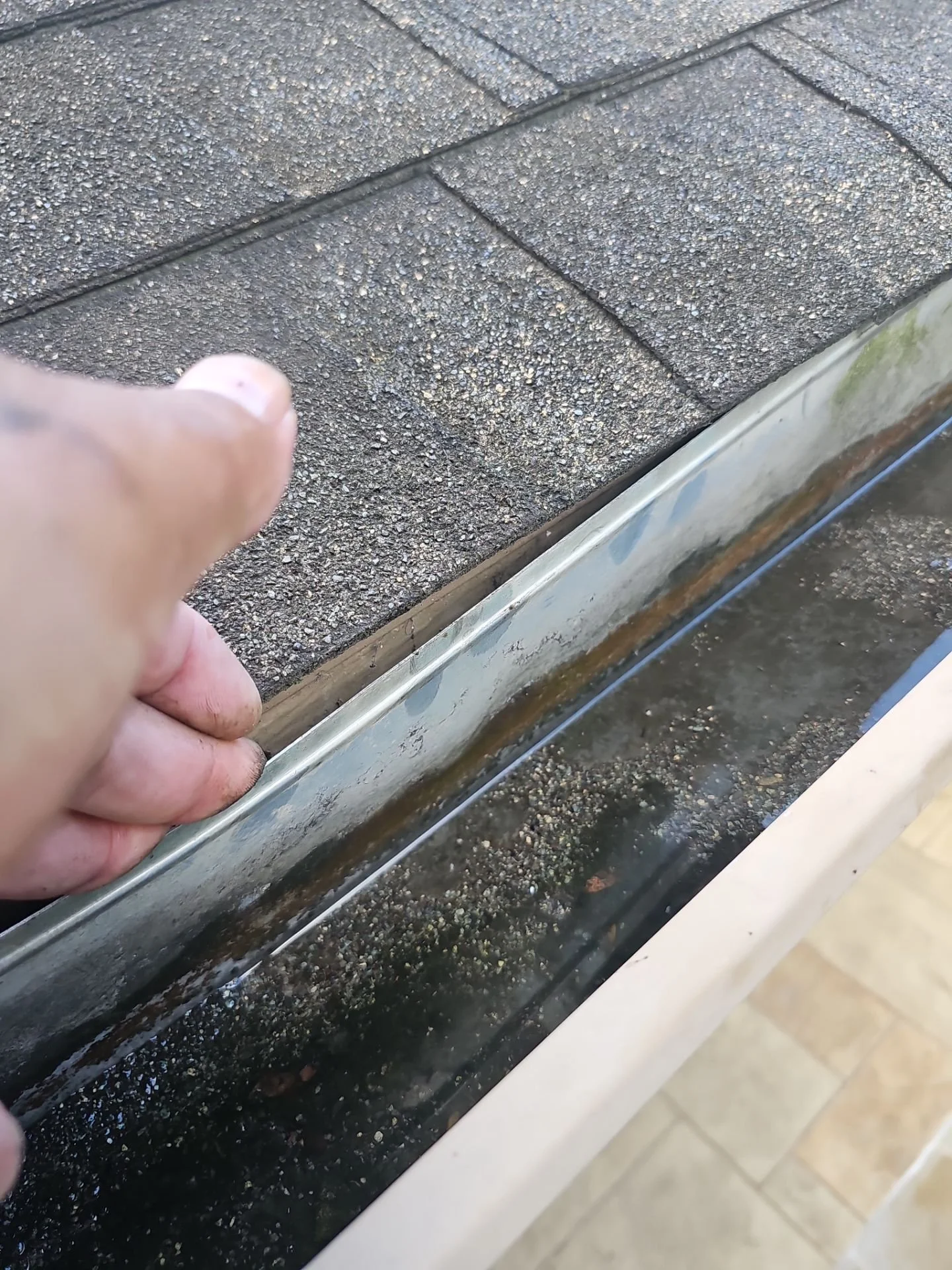 Close-up of a person's hand removing a dirty metal drip edge from a roofing gutter.