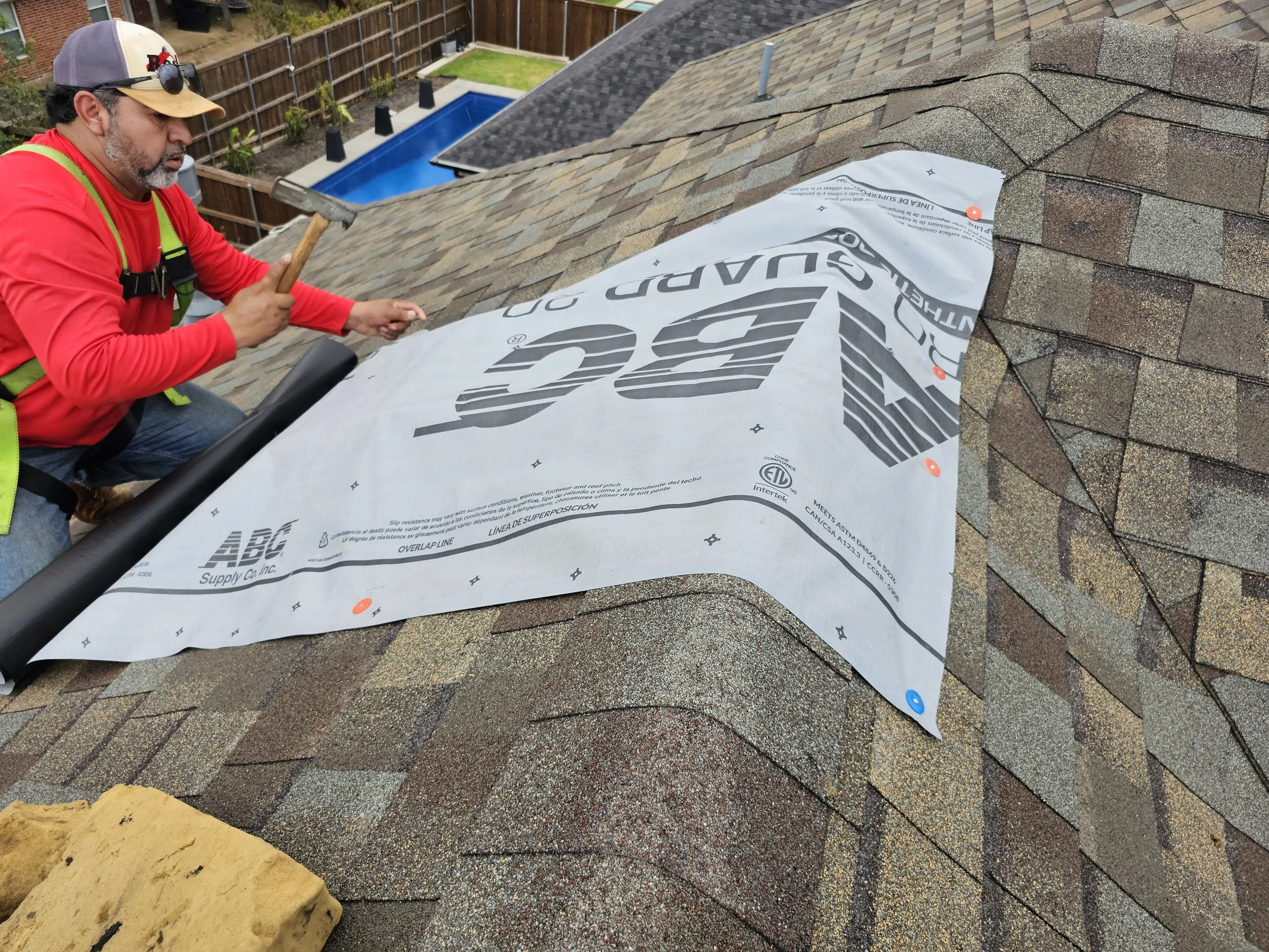 A man working on a house roof, installing new roofing material, with shingles and roofing underlayment visible.