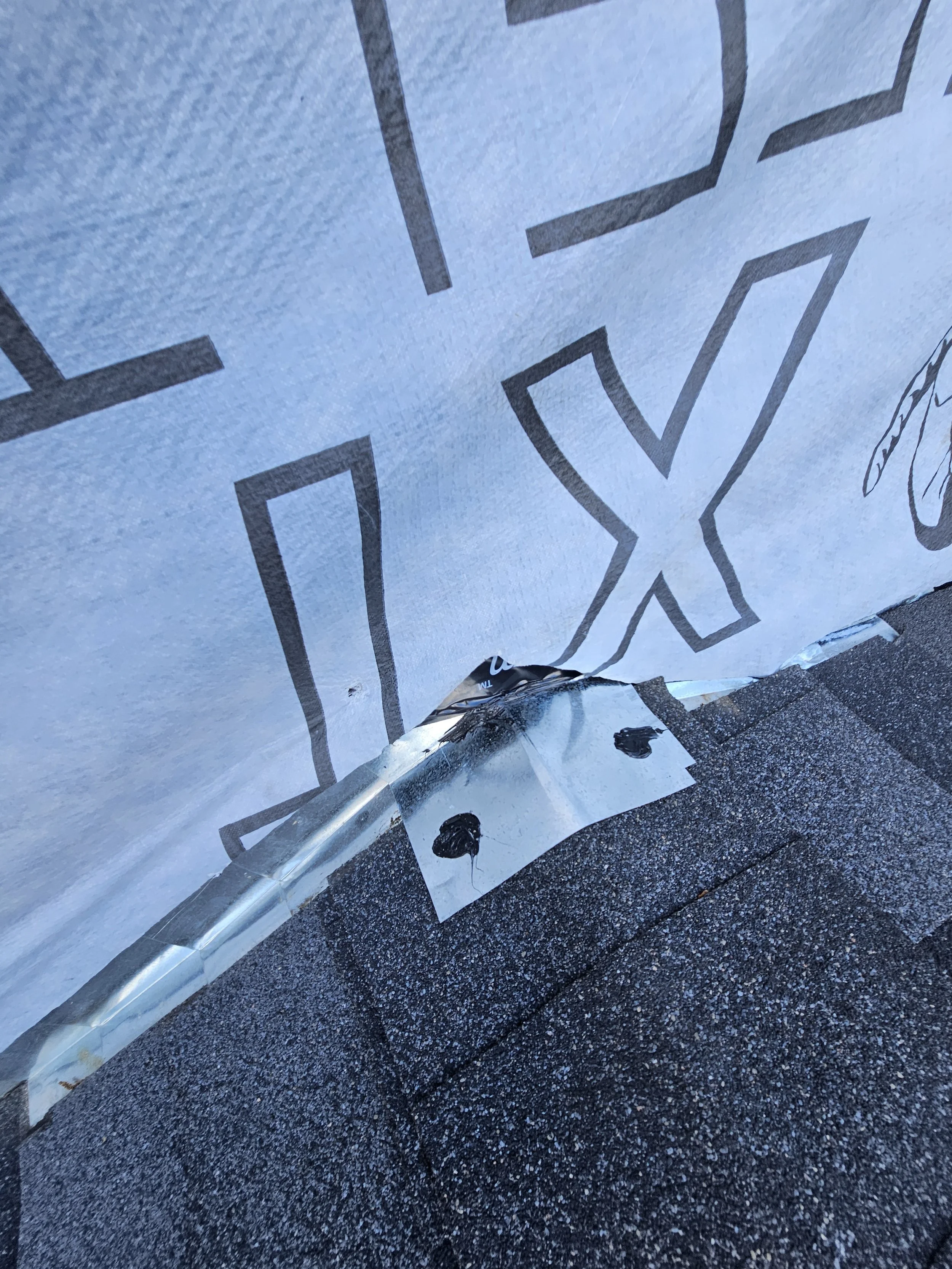 A close-up of a painted surface with black lines and check mark symbols, damaged and peeling at the bottom edge, over a rough asphalt ground.