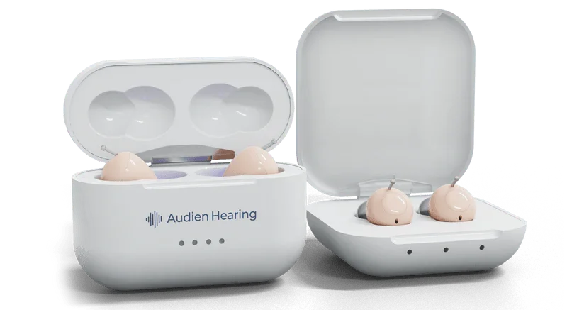 Over-the-counter hearing aids and their charging cases on a black surface.