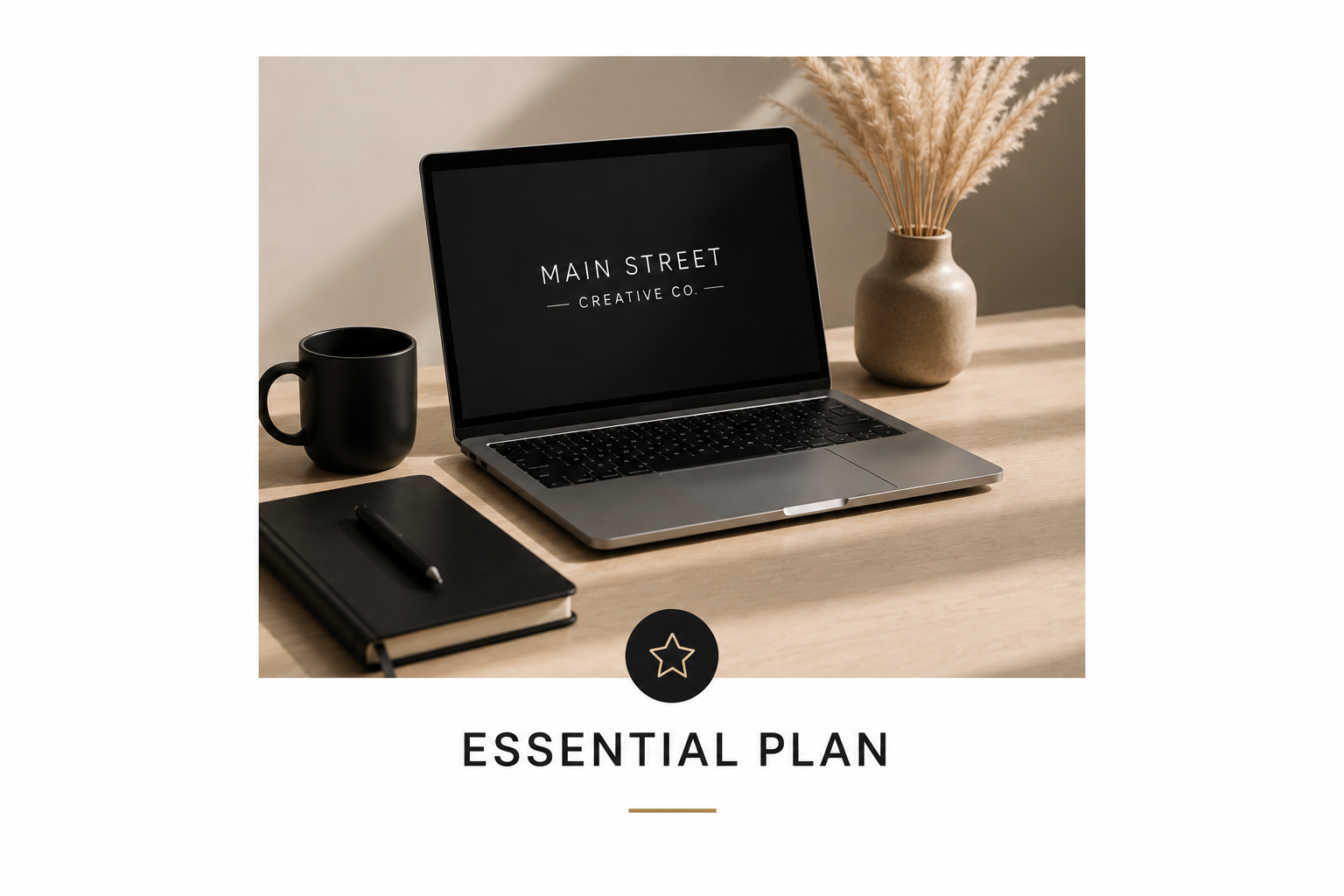 A workspace with a laptop, black coffee mug, black notebook with a pen, and a vase with beige pampas grass on a wooden desk.