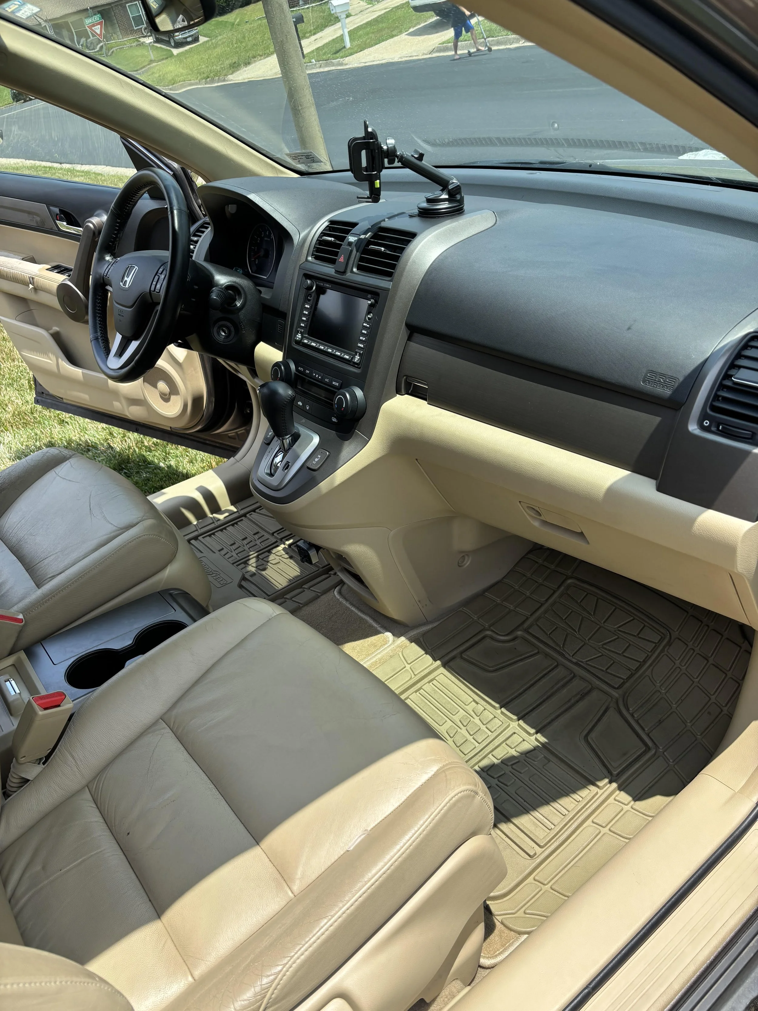 Inside a car showing the front passenger and driver seats with beige leather upholstery, a dashboard with a GPS or multimedia screen, and a mounted phone holder on the dashboard.