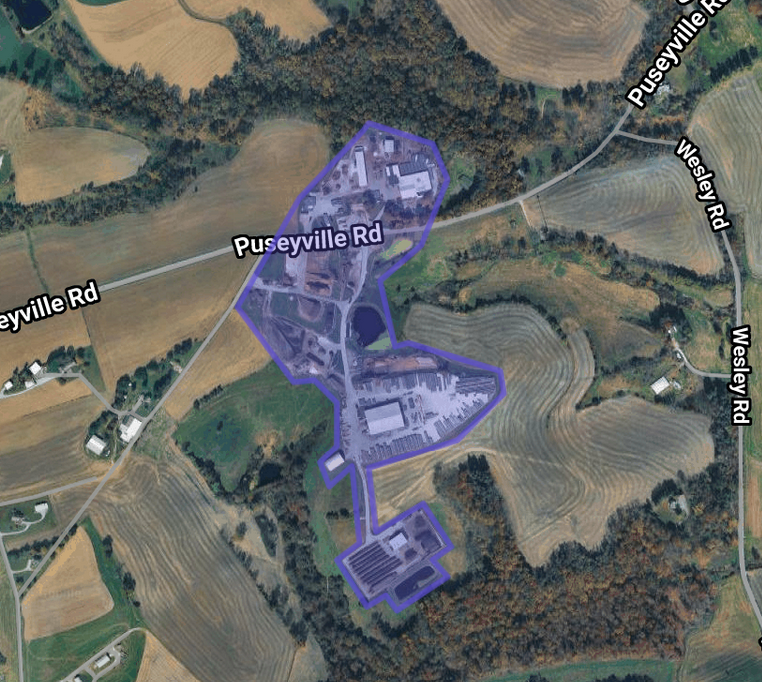 Satellite view of a rural area with fields, roads, and a marked zone outlined in purple, showing buildings and surrounding landscape.