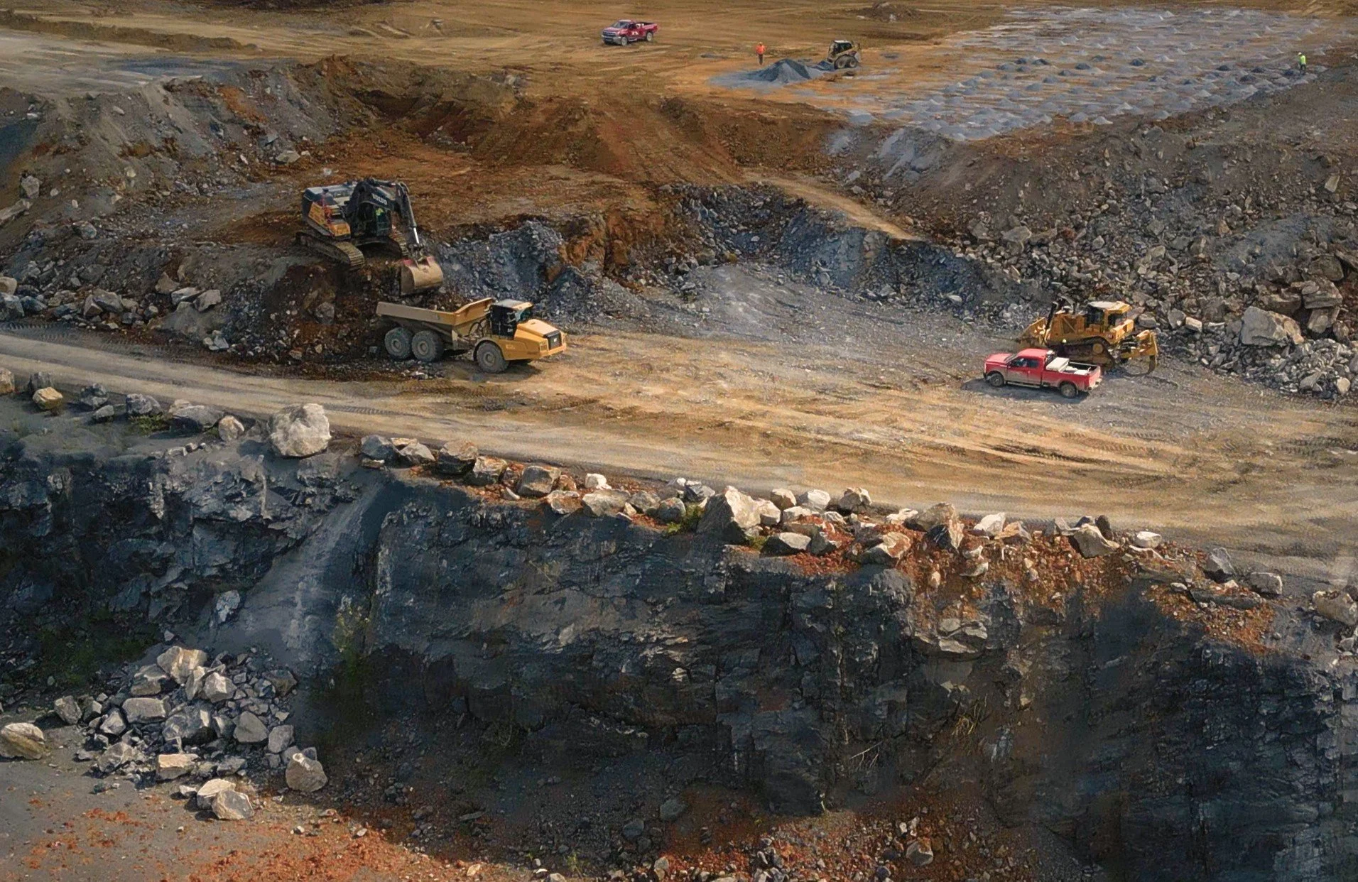 Construction site with excavators, dump trucks, and pickup trucks working on digging and moving earth and rocks
