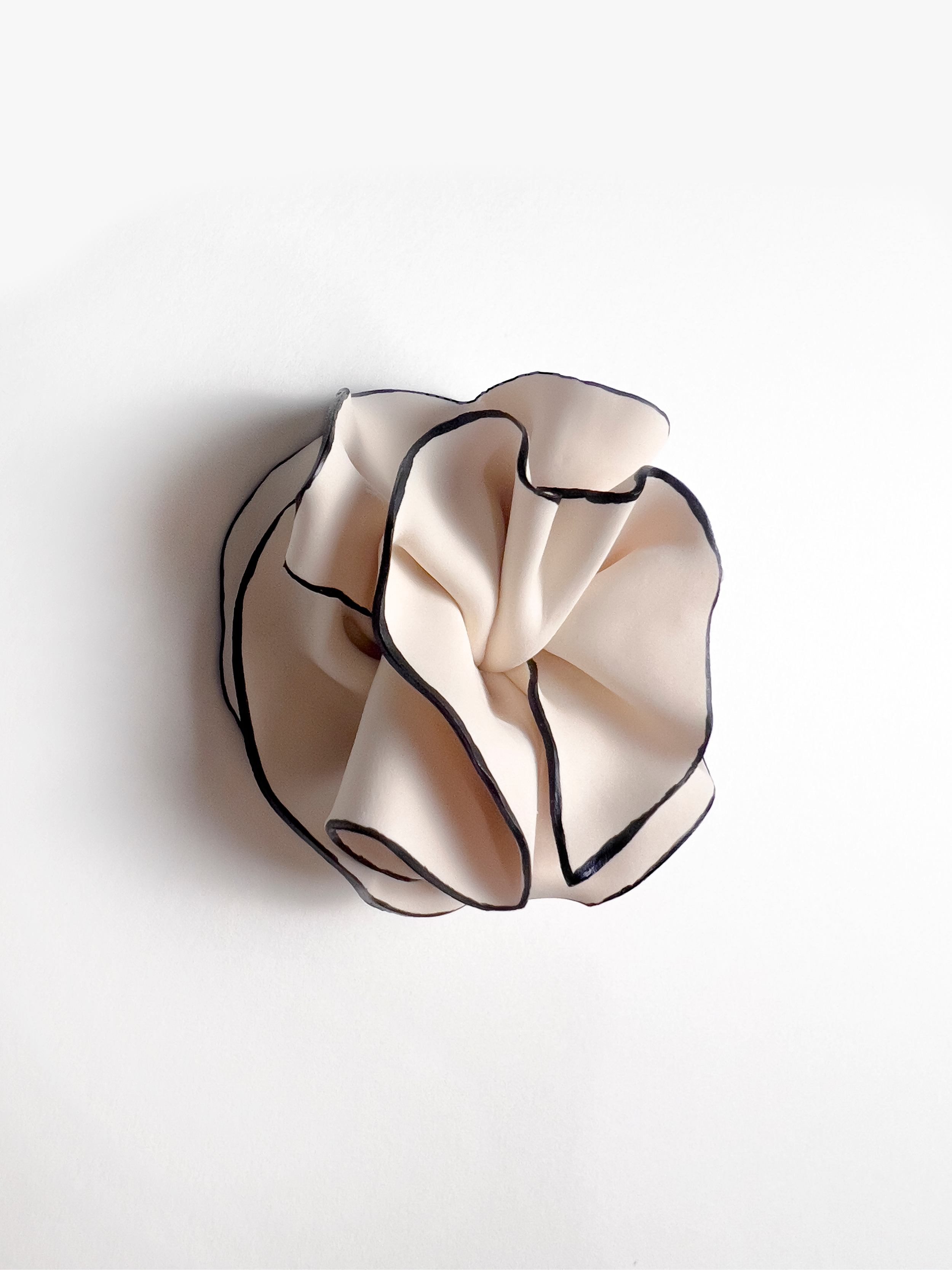 A close-up of a beige fabric scrunchie with black trim, resting on a white surface.