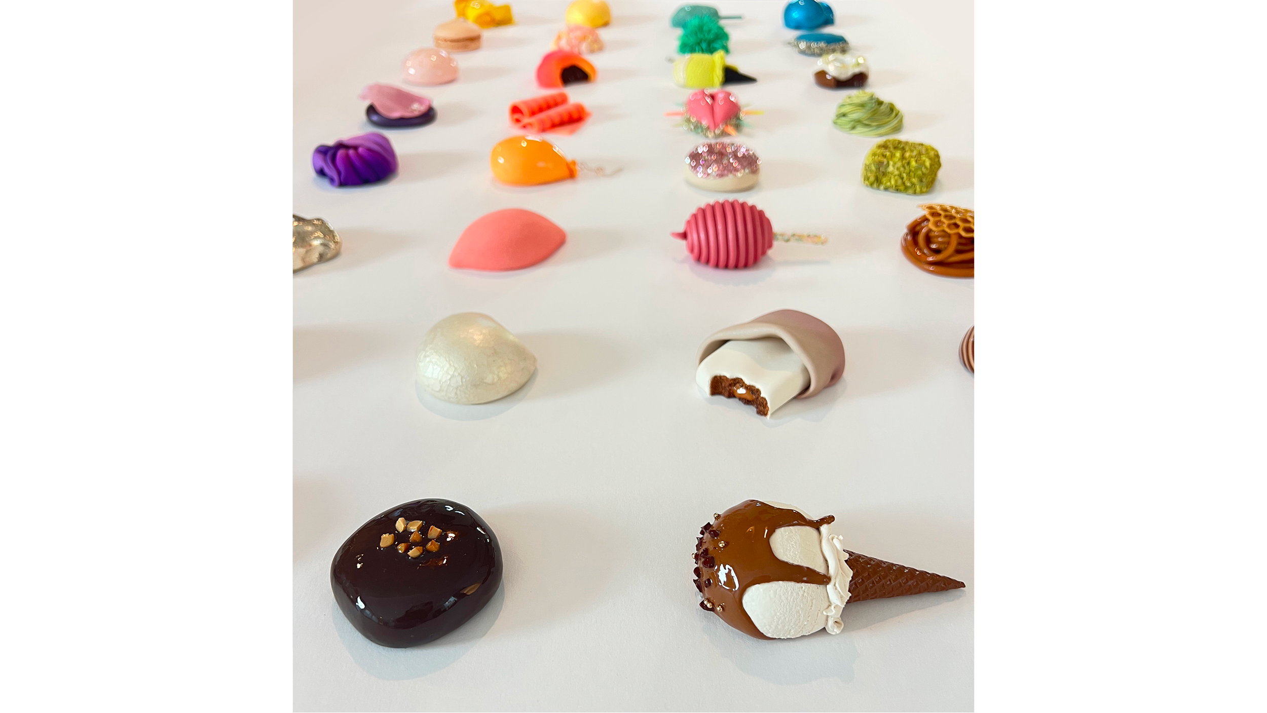 A variety of colorful polymer clay crafted objects arranged on a white surface, including fruits, flowers, and abstract shapes.