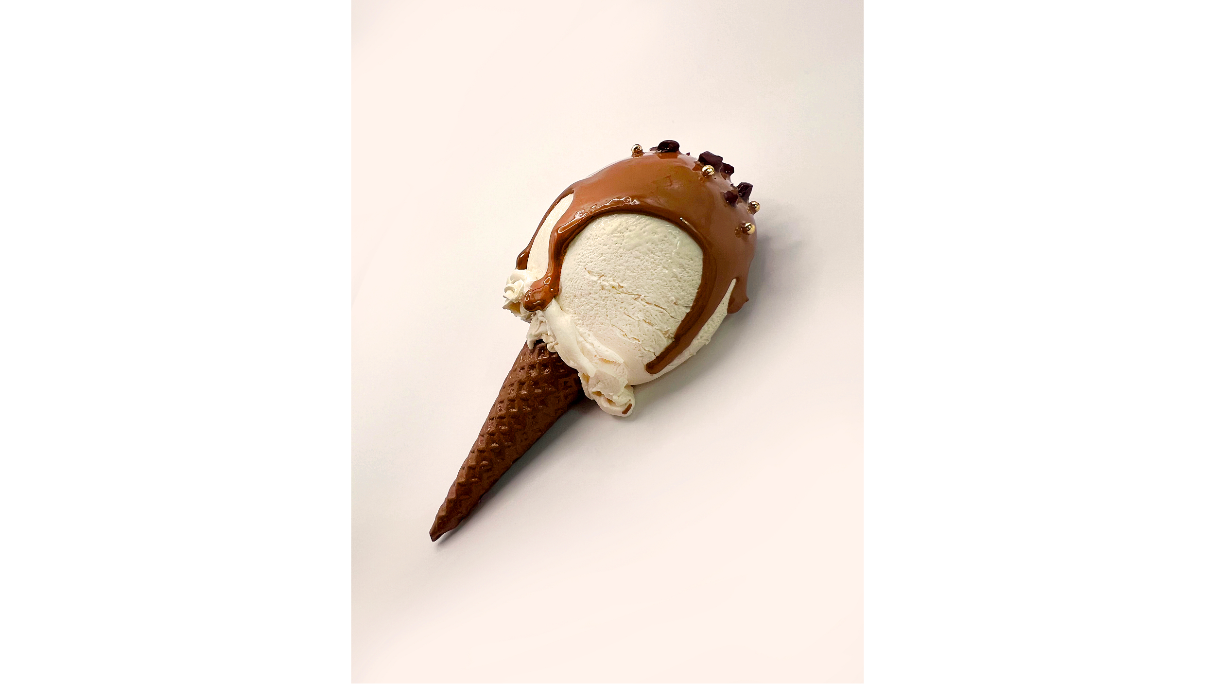 A single scoop of vanilla ice cream topped with chocolate sauce and small chocolate pieces, served in a waffle cone against a plain white background.