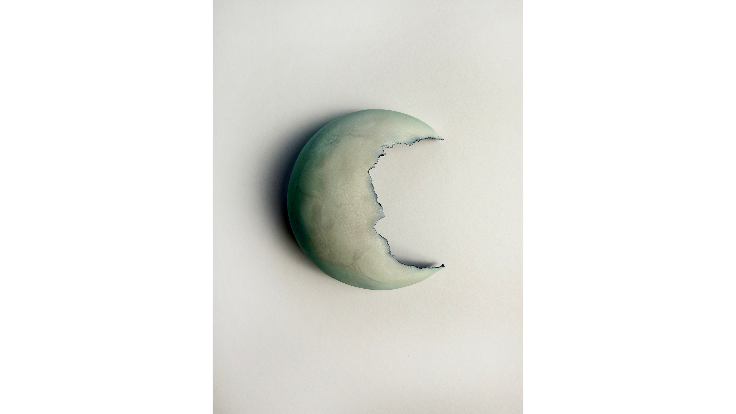 A greenish, marble-like crescent-shaped object with a jagged edge, on a plain white background.