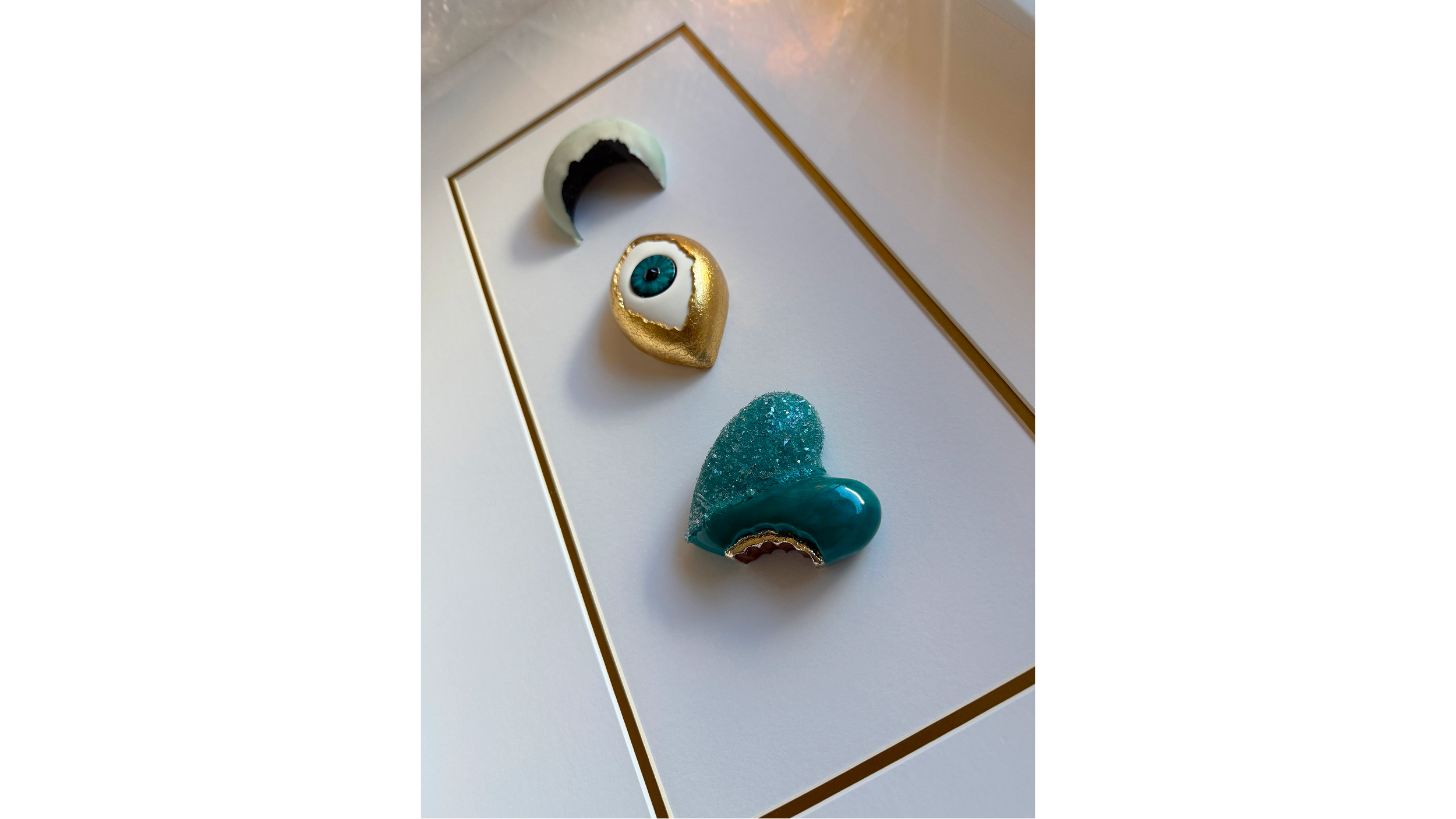 Artistic mixed media pieces include a crescent moon, a stylized eye, and abstract shapes on a white surface with a gold frame.