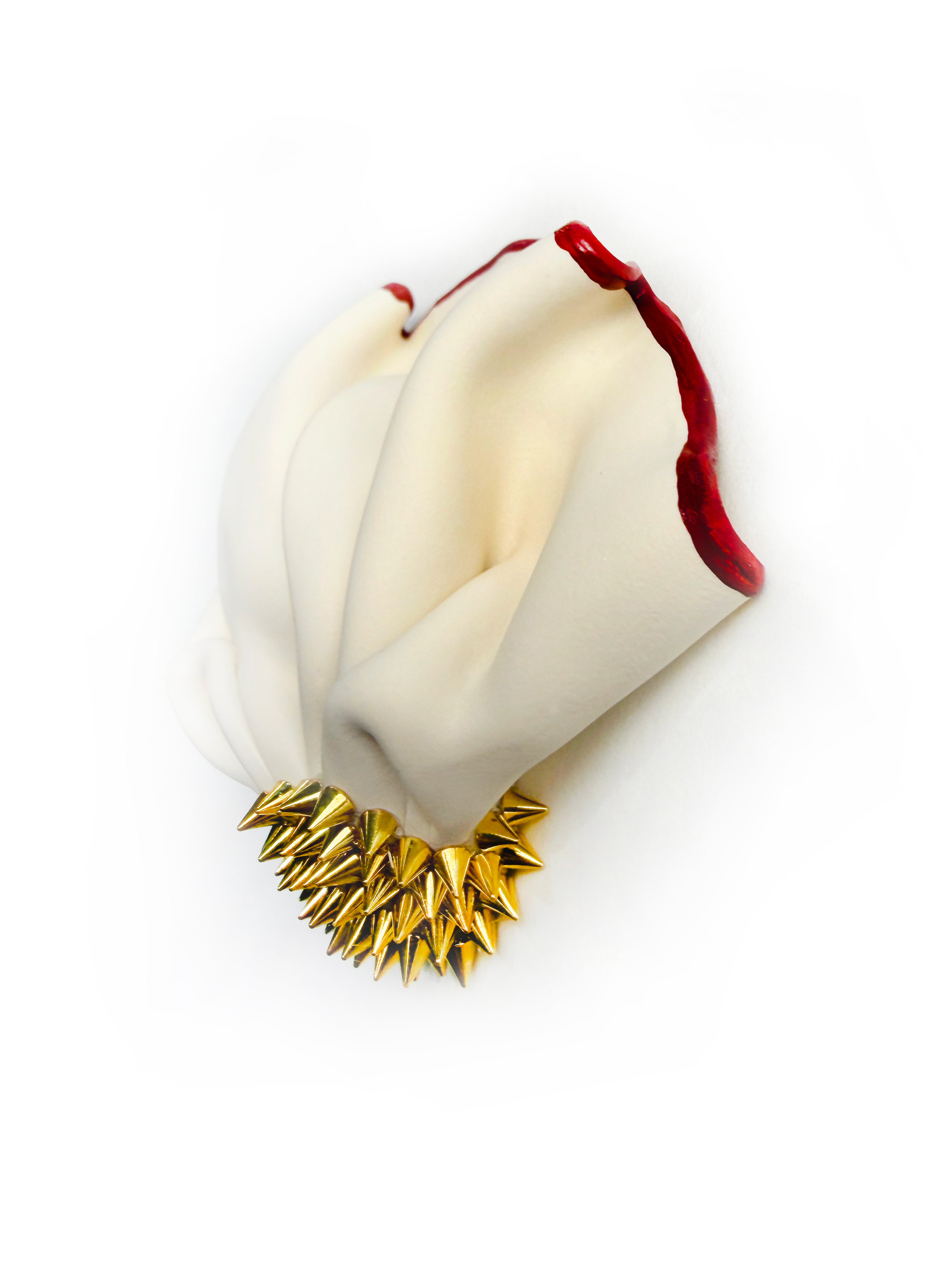 Close-up photograph of a white, folded designer garment with red detail along the edges, accessorized with a gold spike necklace.