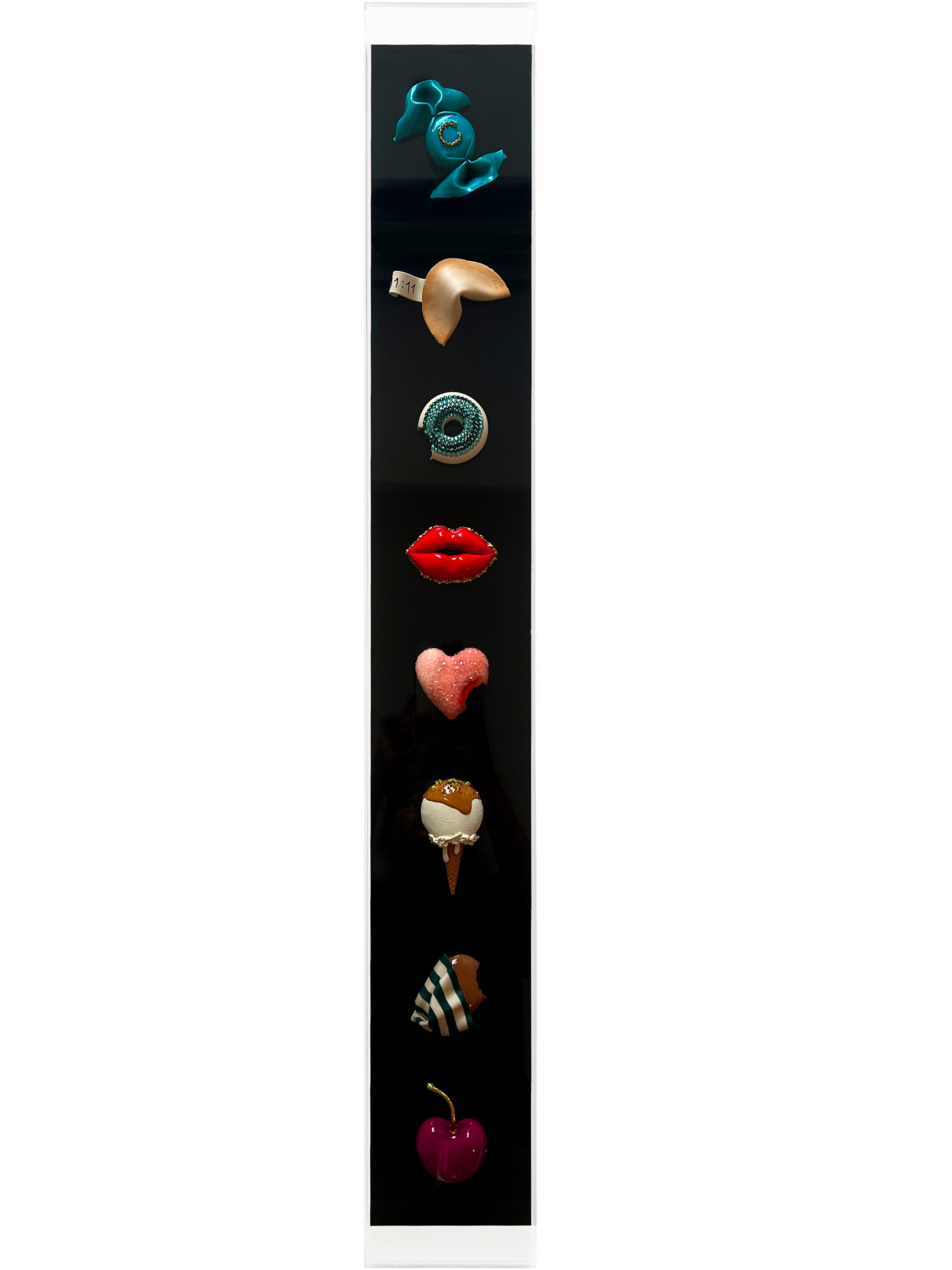 A vertical display case with various whimsical objects, including a red lips sculpture, an ice cream cone, a chocolate bar, a pink heart, a cherry, a star, a piece of cake, a wrapped candy, a bow, and a pair of cherries, arranged from top to bottom.