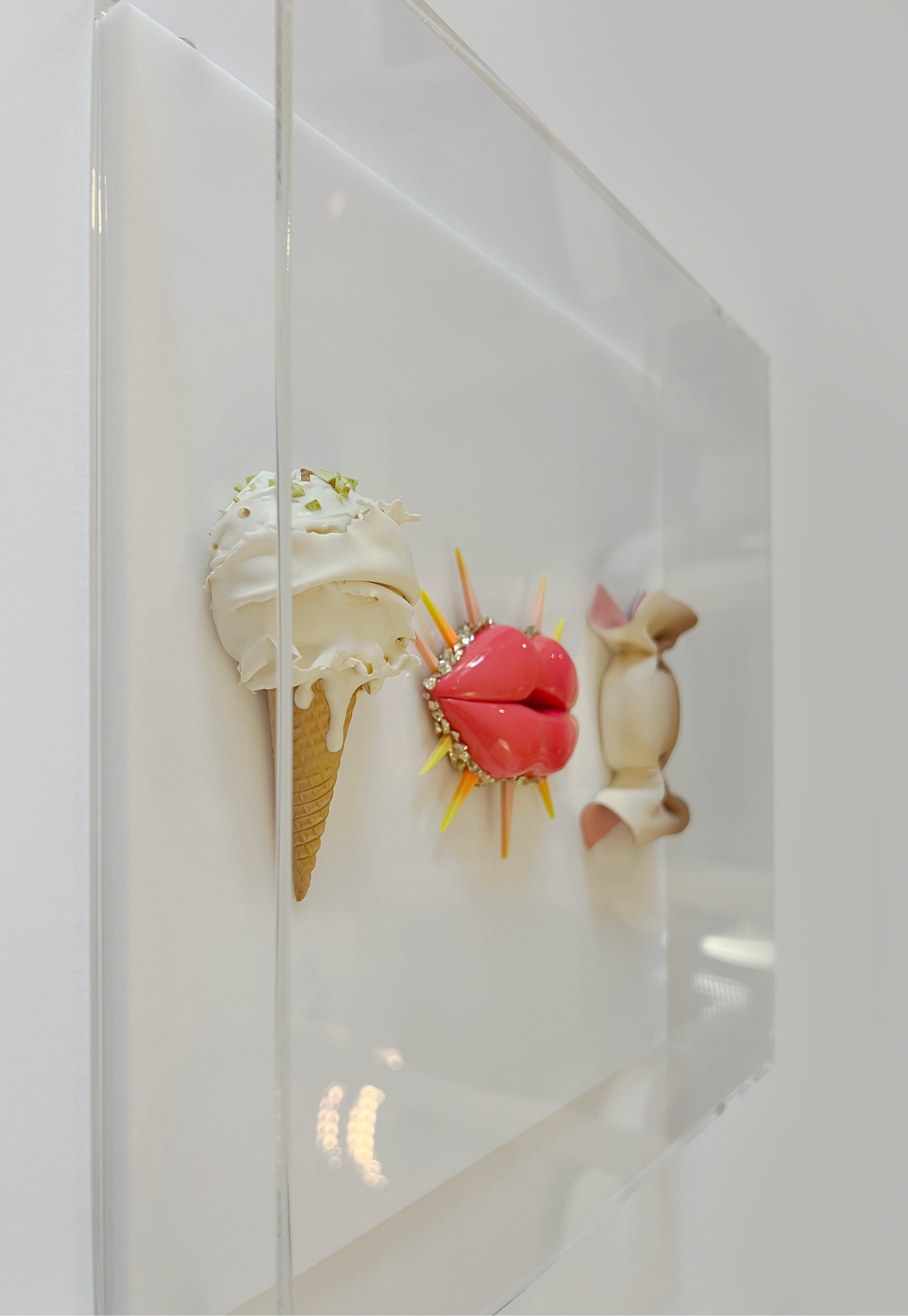 Decorative wall display of three artistic ice cream and dessert sculptures on a white wall.