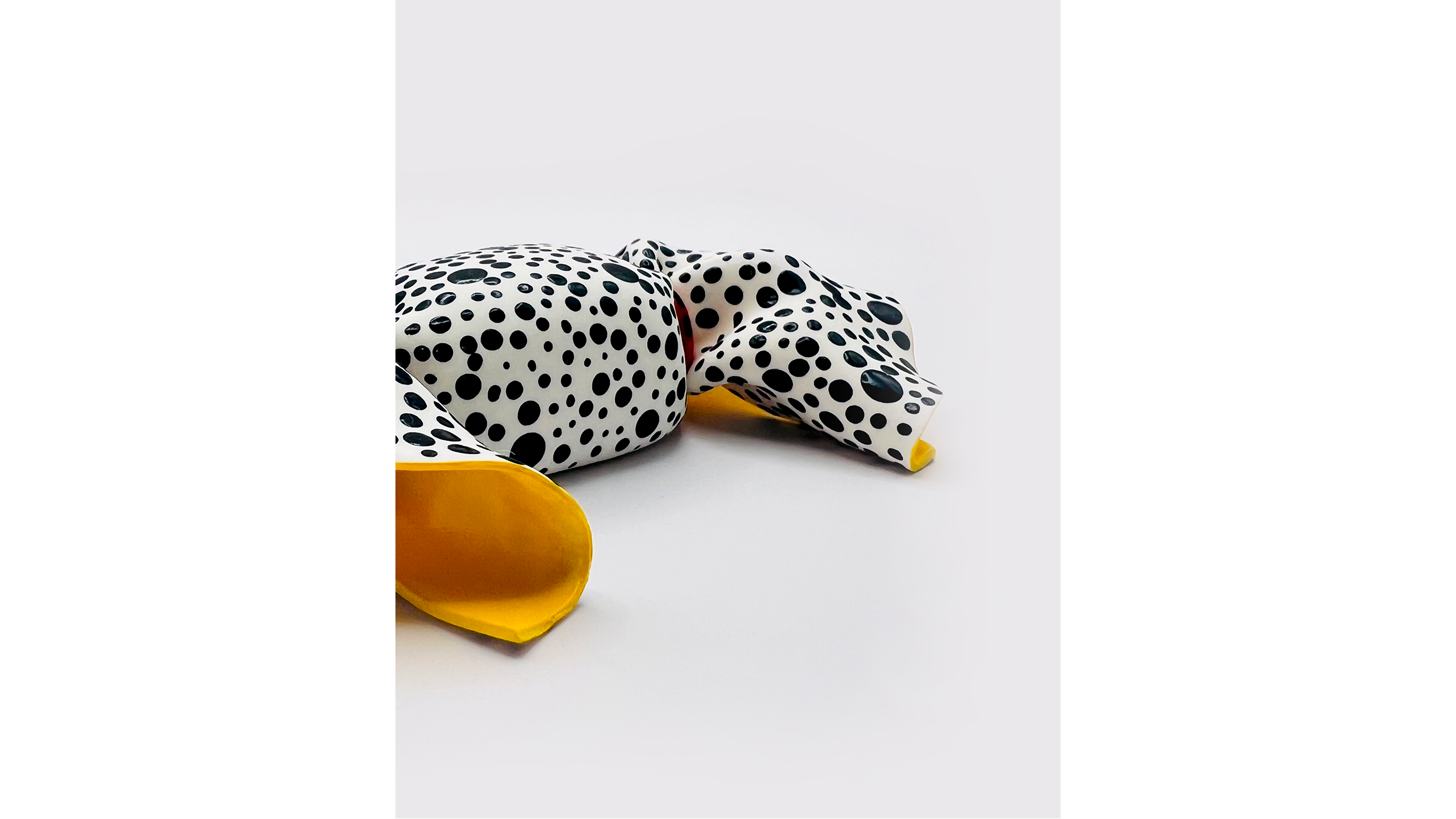 A white object with black polka dots and a yellow base, possibly a decorative item or sculpture, placed on a plain white background.