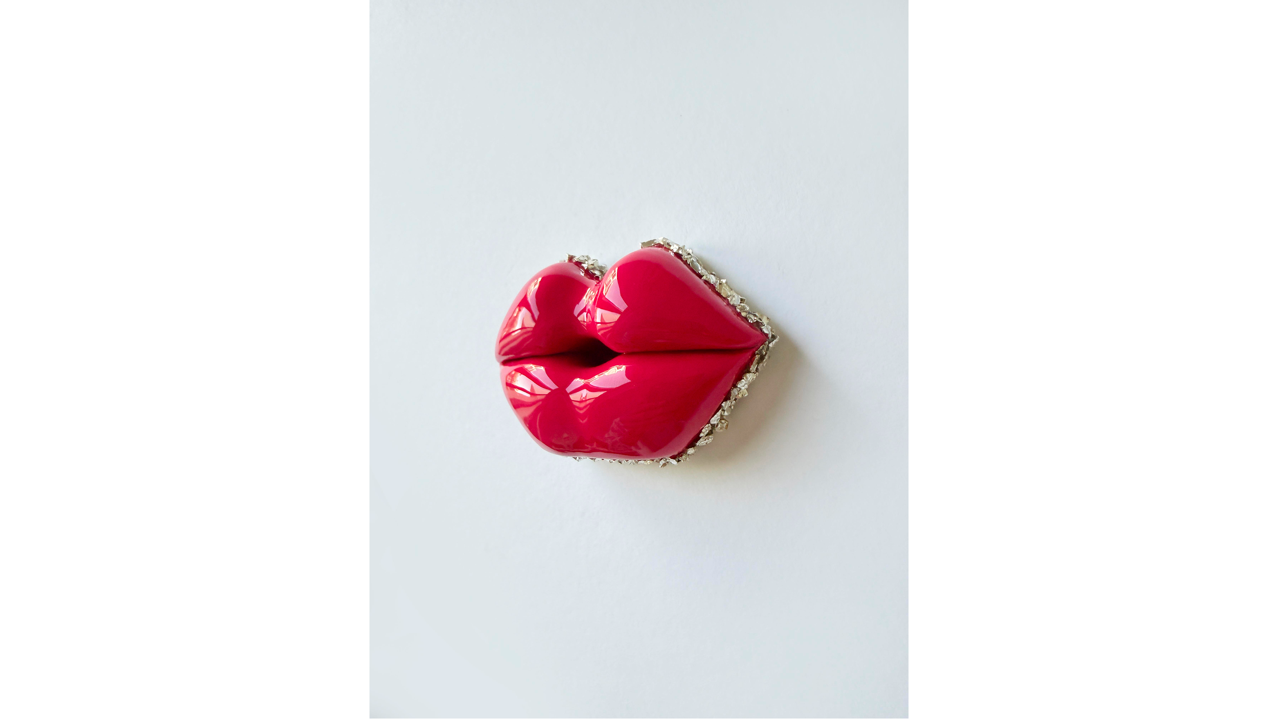 A jewelry pin in the shape of lips painted in glossy pink with a silver rhinestone border.