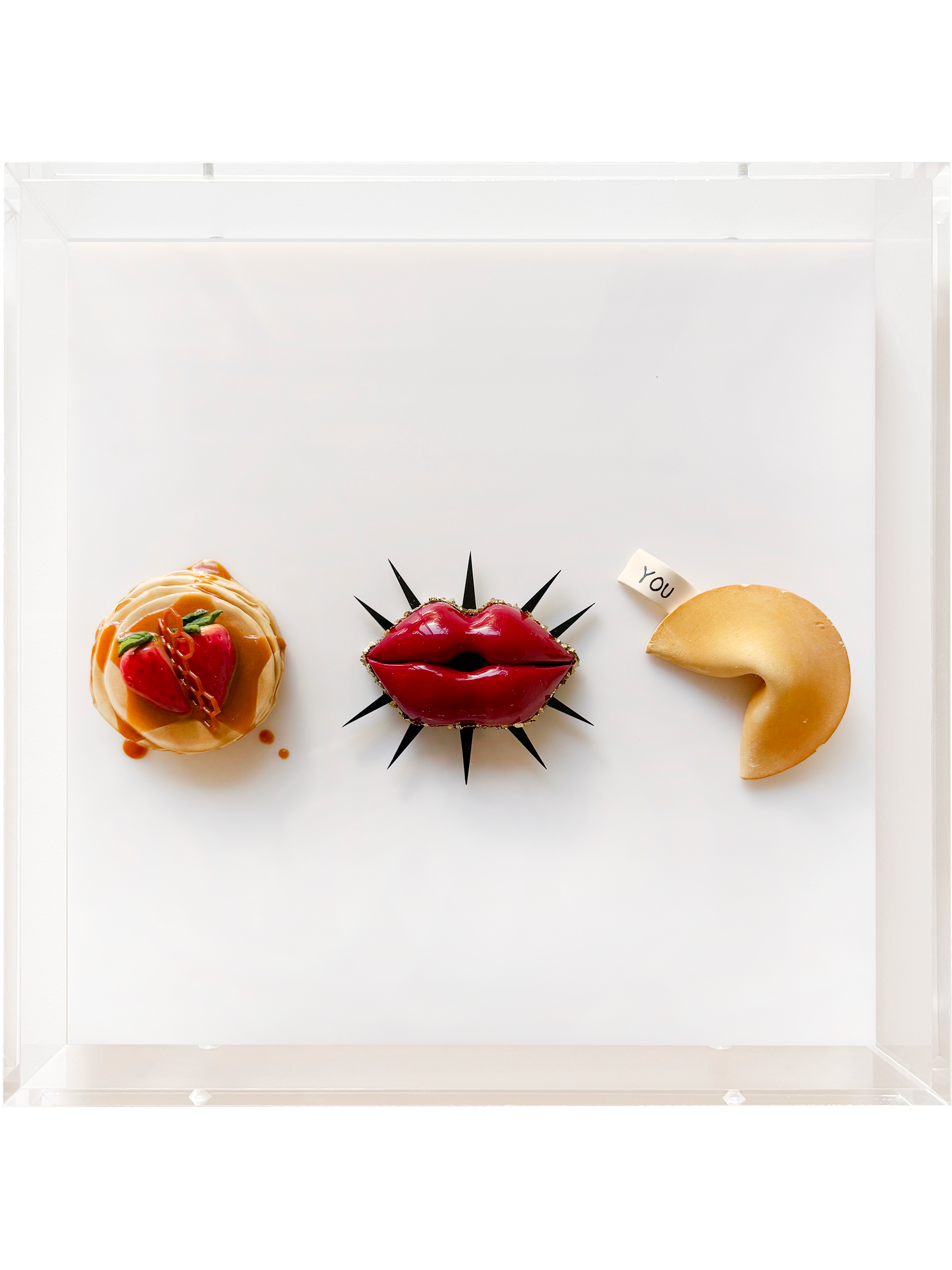 A display of three small sculptures or cakes with different designs, arranged in a row on a white surface, against a white background.