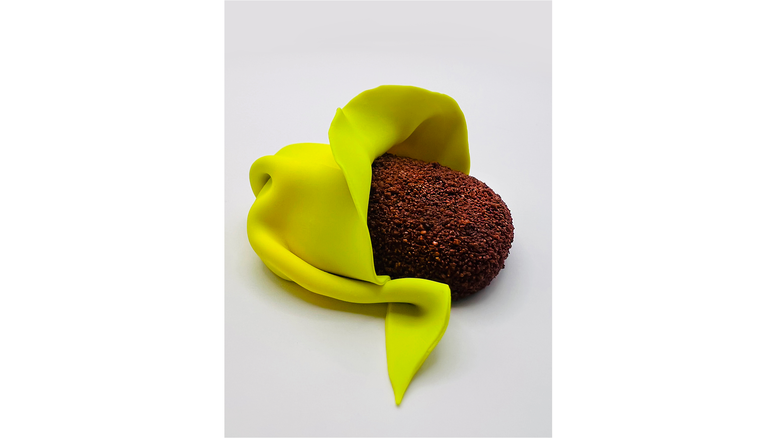 A round, dark brown, textured bread roll partially wrapped in a bright yellow, flexible silicone cover on a white background.