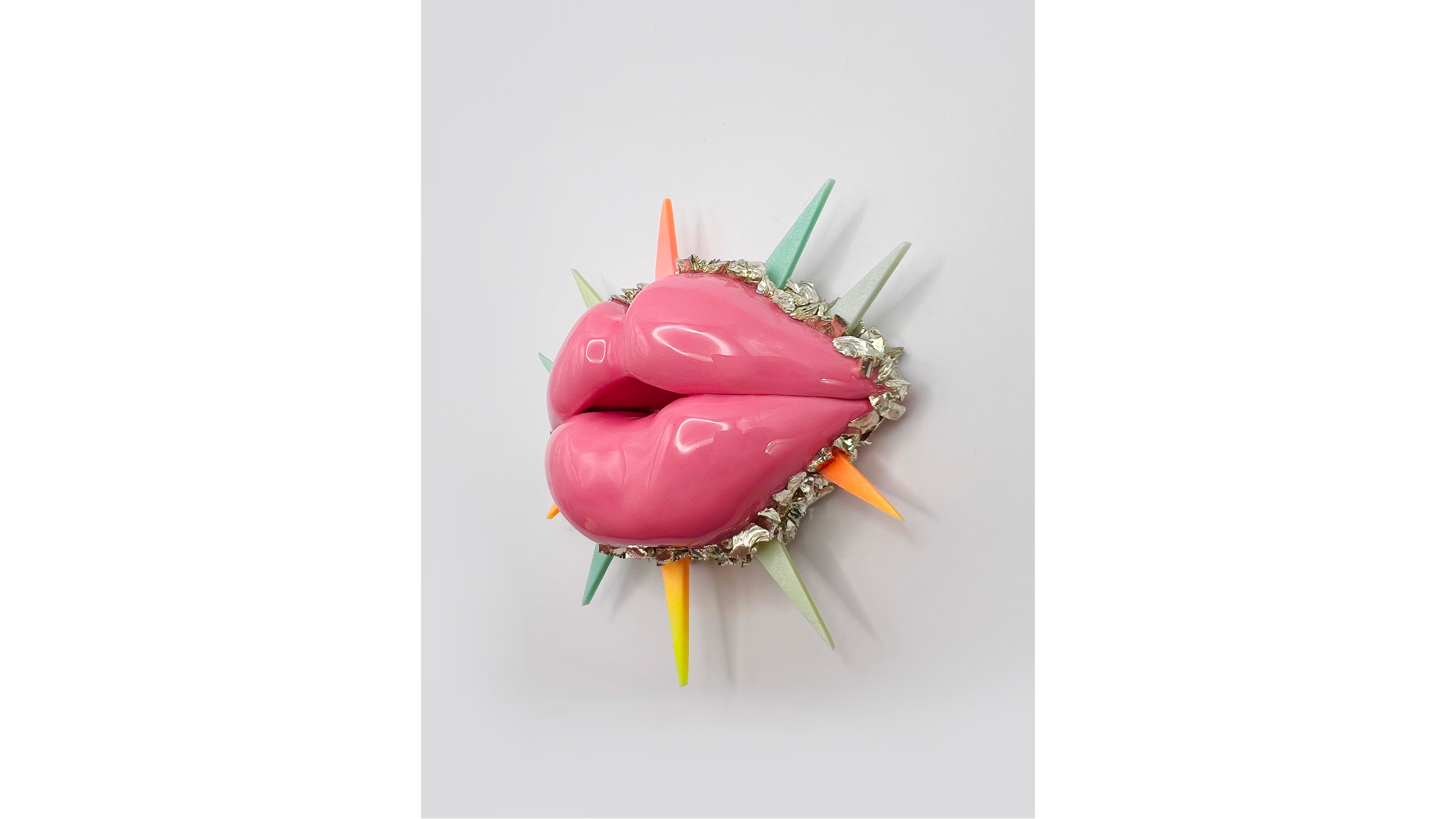 A decorative pink bowl with lips shape, decorated with silver accents and surrounded by colorful triangular sticks, resembling a stylized face or mask.