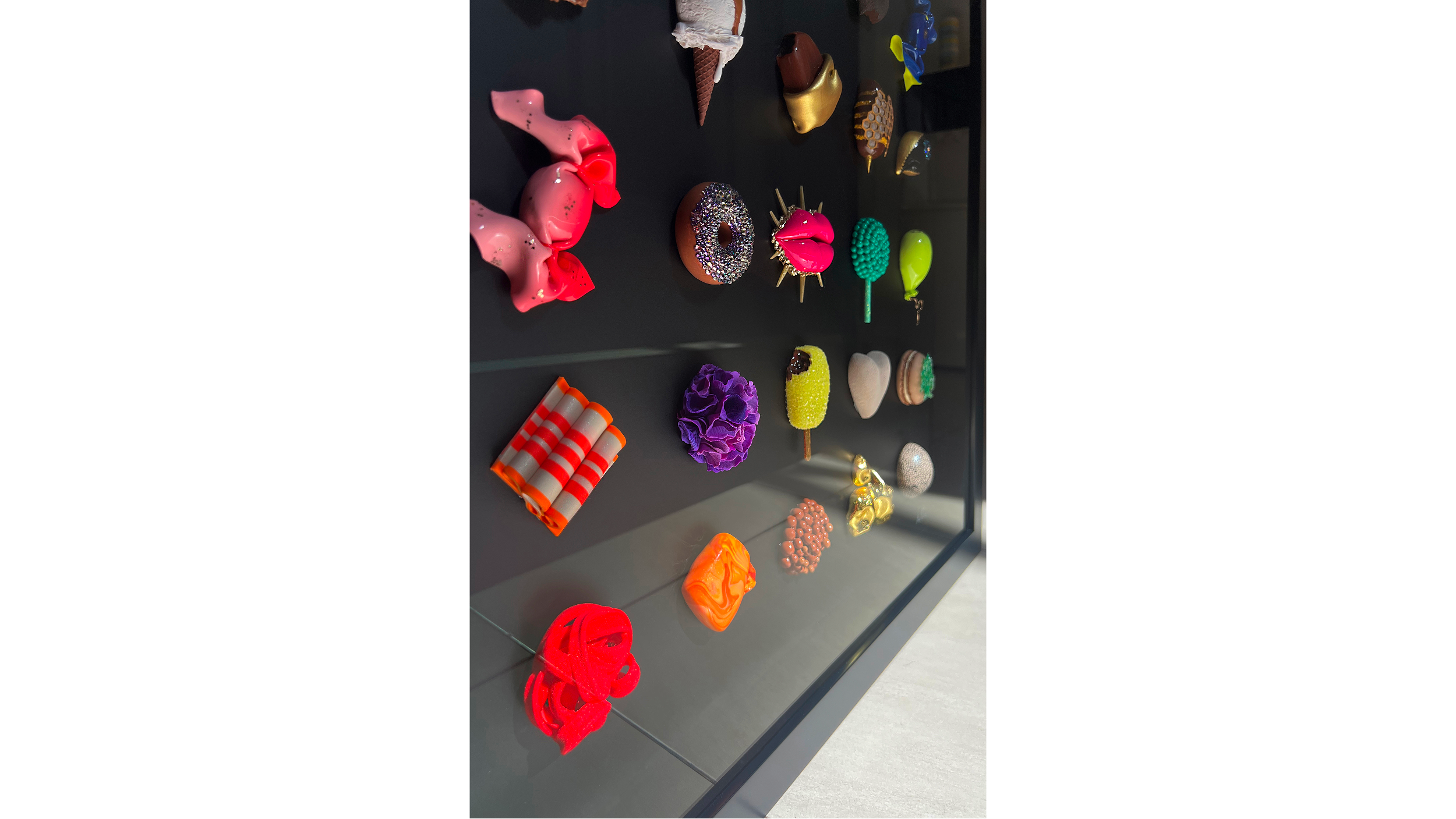 A display of colorful, decorative soaps shaped like various objects including animals, food, and abstract designs on a black surface.