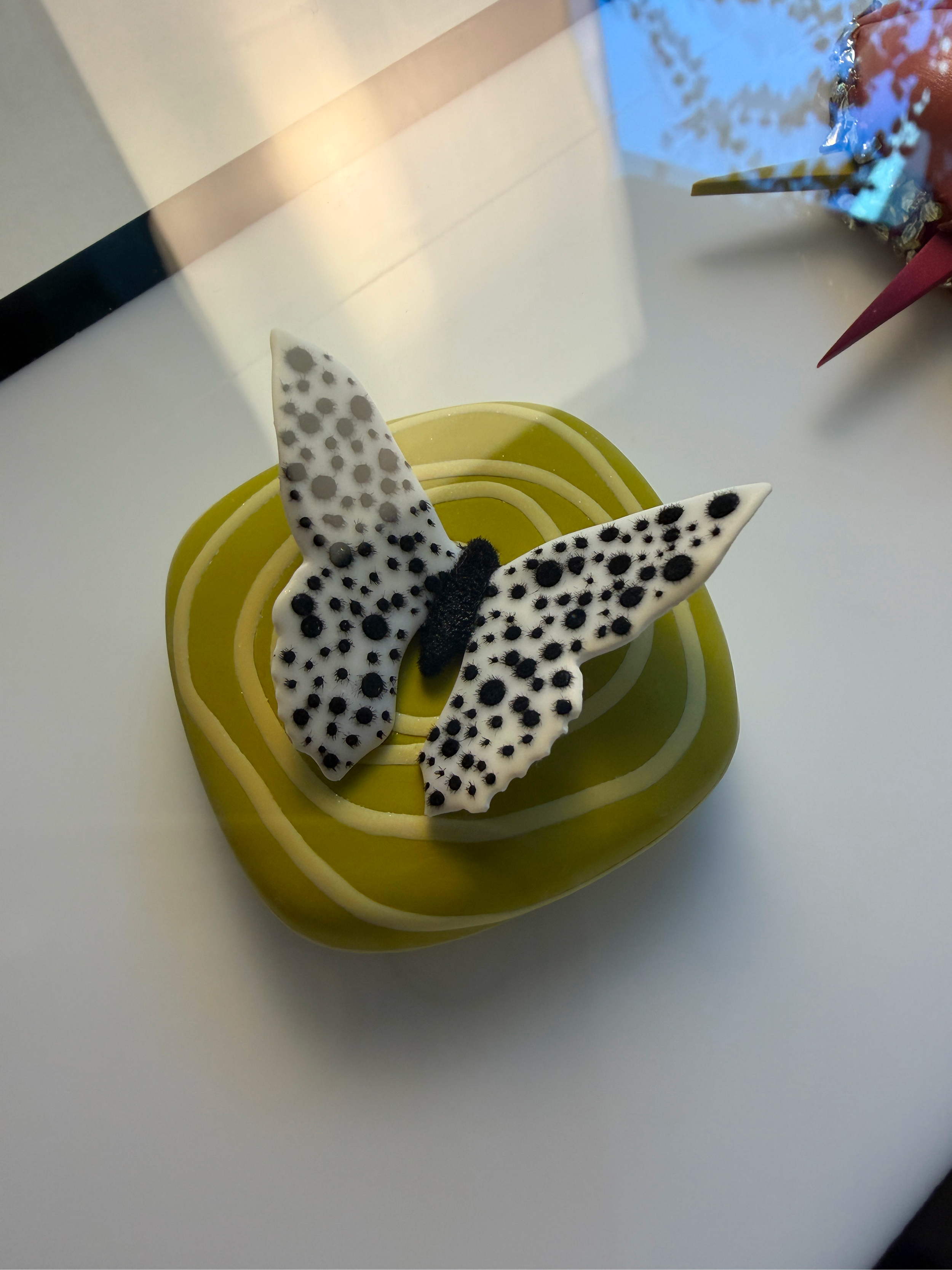 A yellow plate with a white butterfly-shaped decoration covered in black spots, sitting on a white surface.