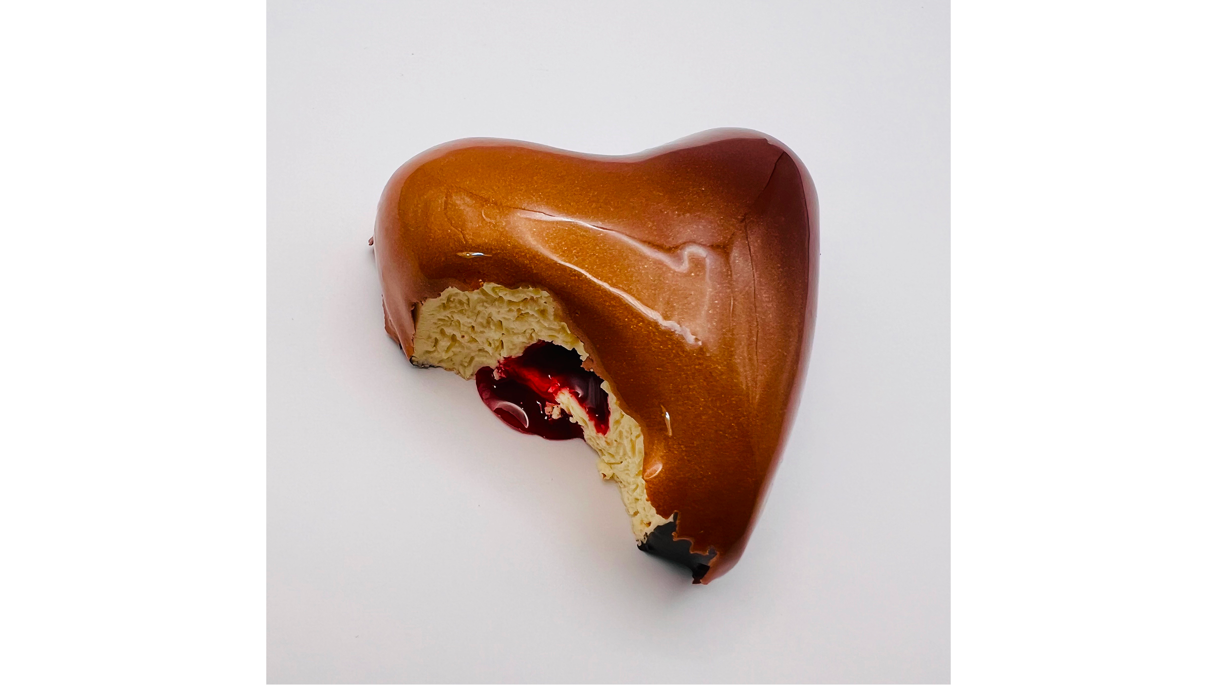 Heart-shaped cake with chocolate glaze and a bite revealing cream filling and red jam center on white background.