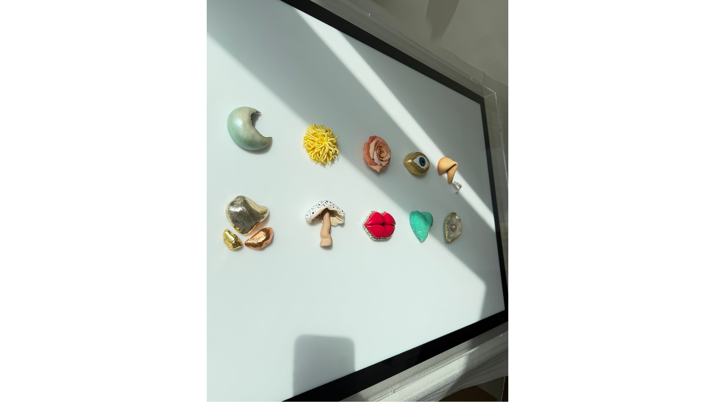 Collection of decorative objects resembling various shapes including a crescent moon, a head with curly hair, an eye, lips, and abstract forms, arranged on a white surface with shadows.