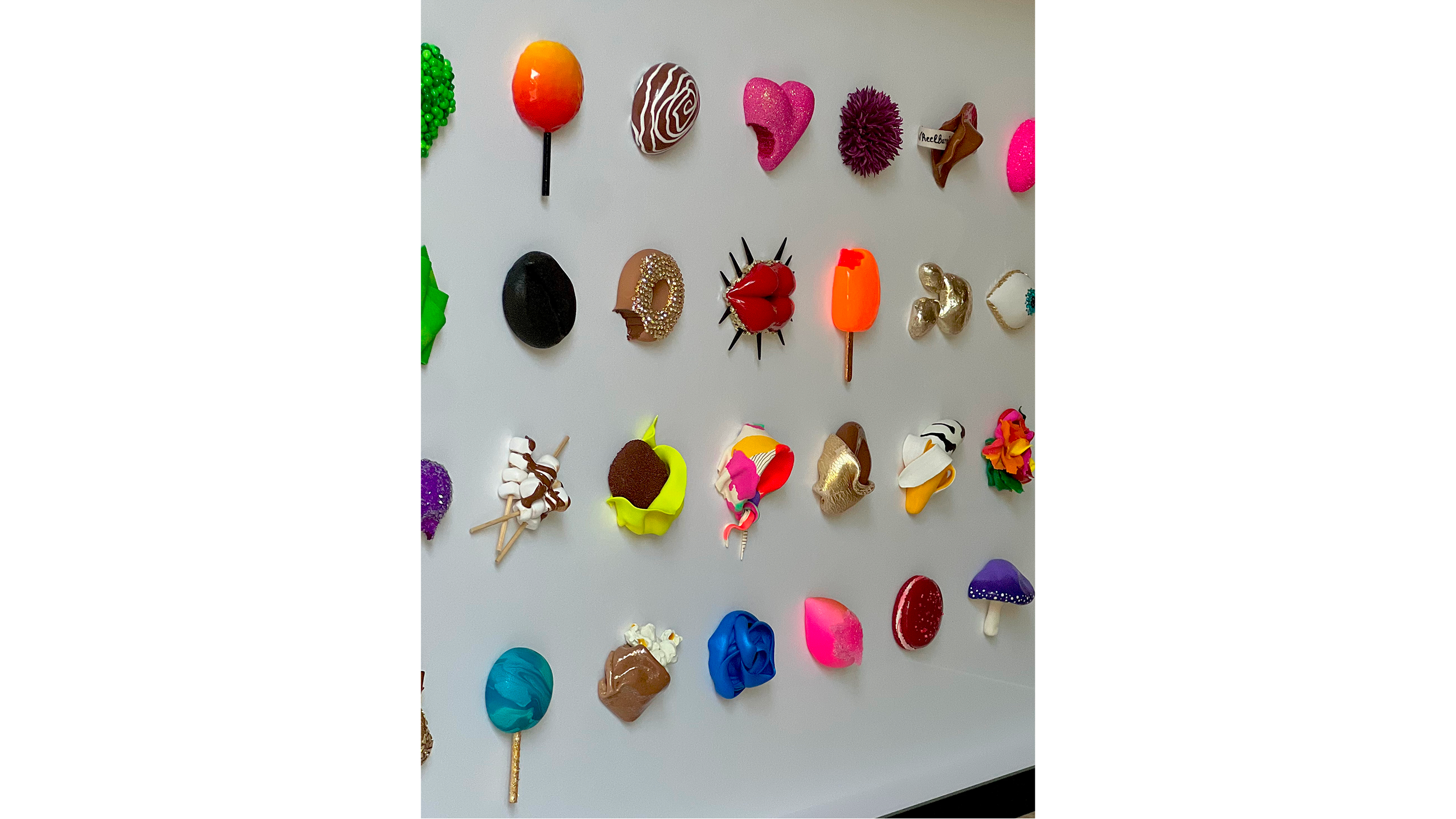 A display of various colorful, decorative plastic or foam dessert replicas including lollipops, chocolates, and candies arranged on a white surface.