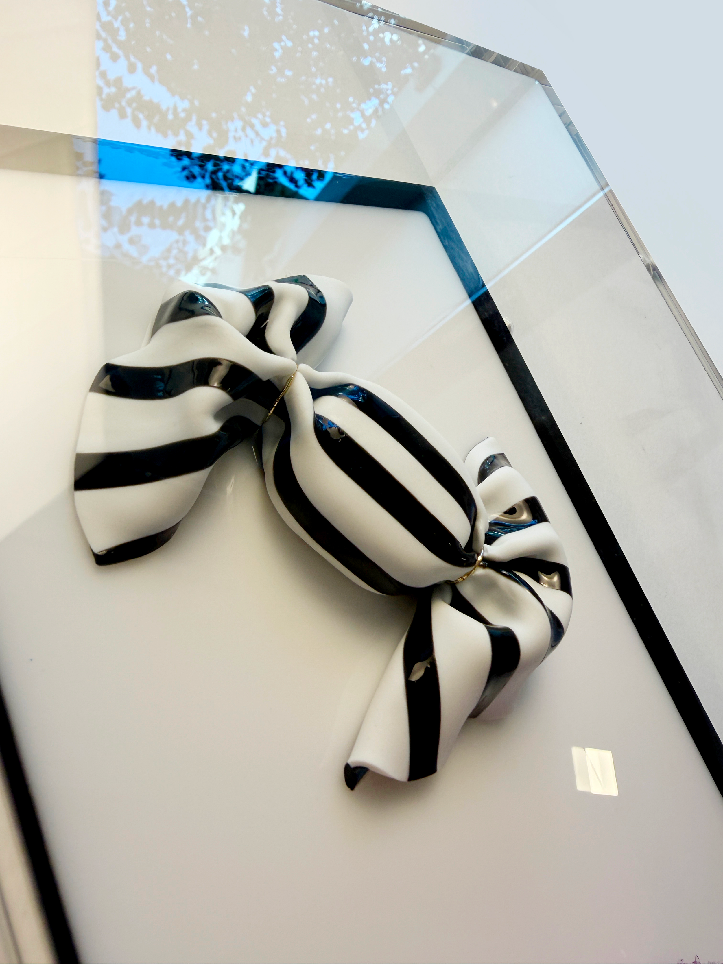 Close-up photo of a black and white twisted ribbon on a white surface, with a mirror reflecting a window and a tree outside.