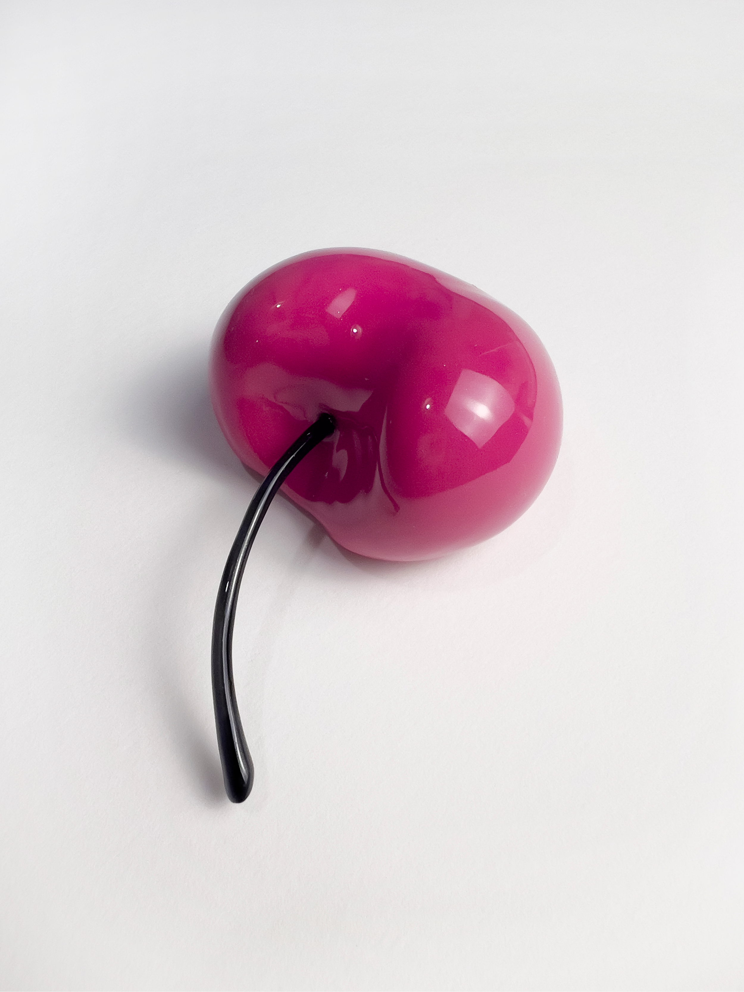 A pink, shiny purse with a black handle on a white surface.
