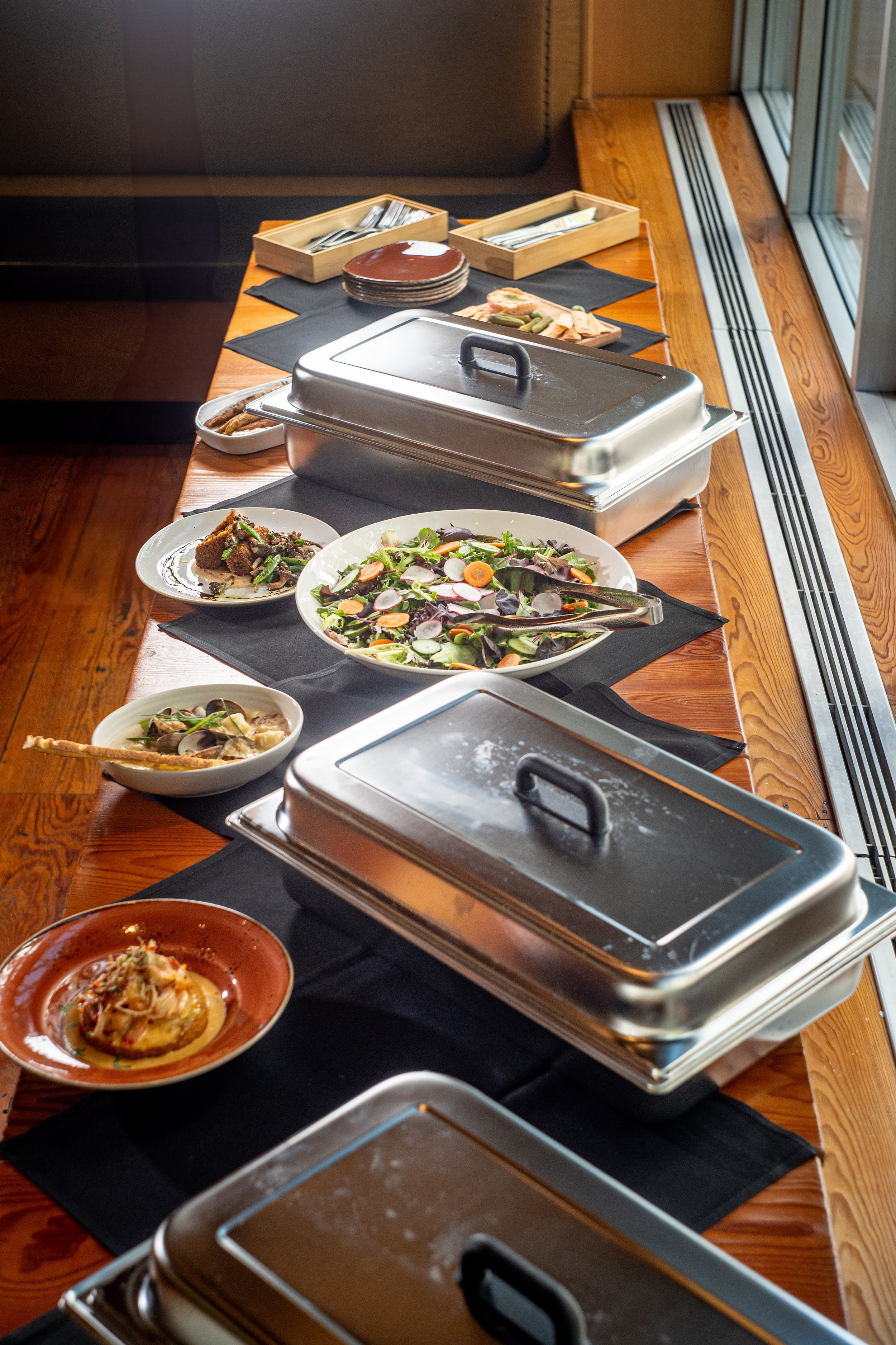 Buffet table with various dishes including salads, pasta, and cooked items, with chafing dishes and serving utensils.