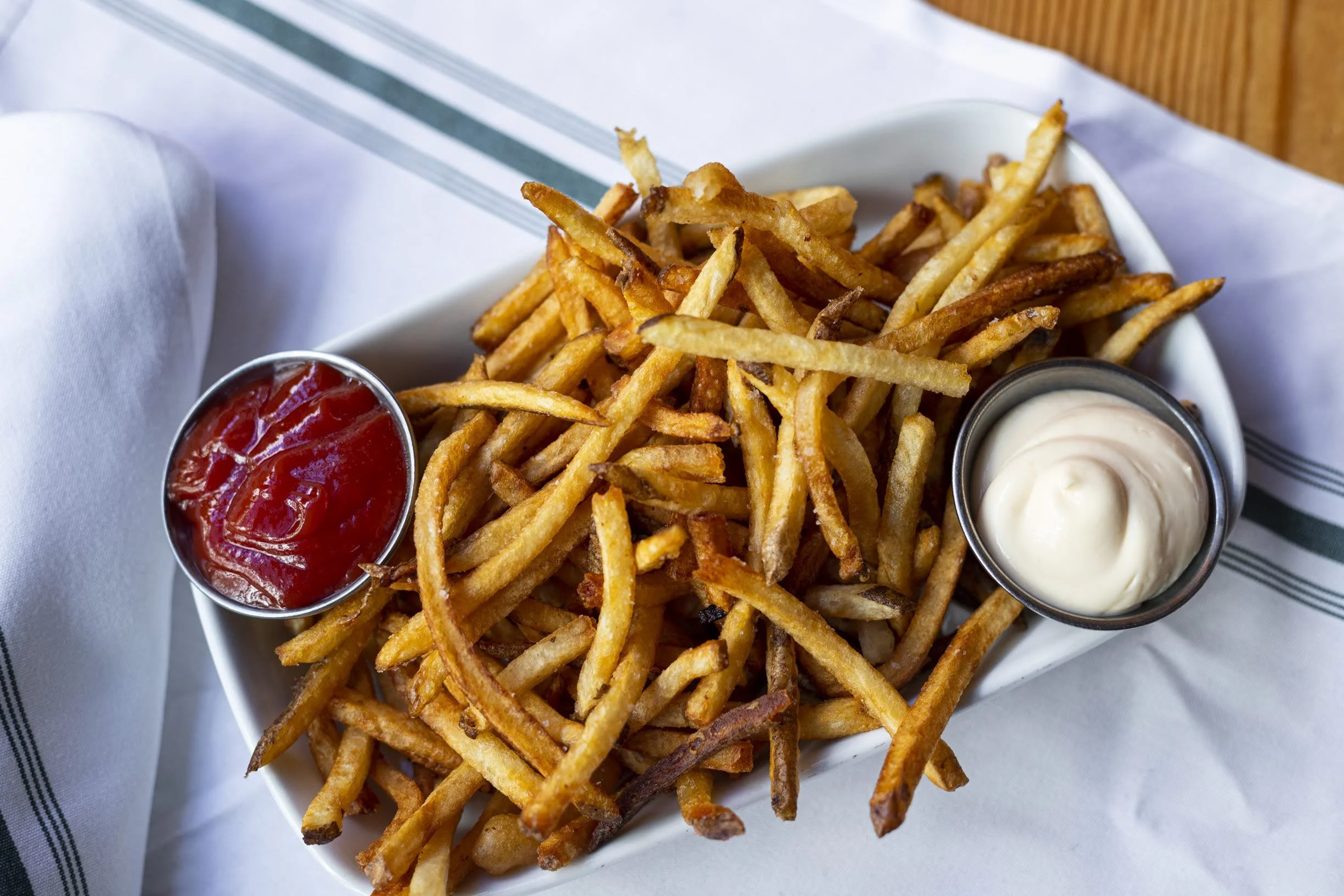 A white rectangular dish filled with French fries served with ketchup and mayonnaise.