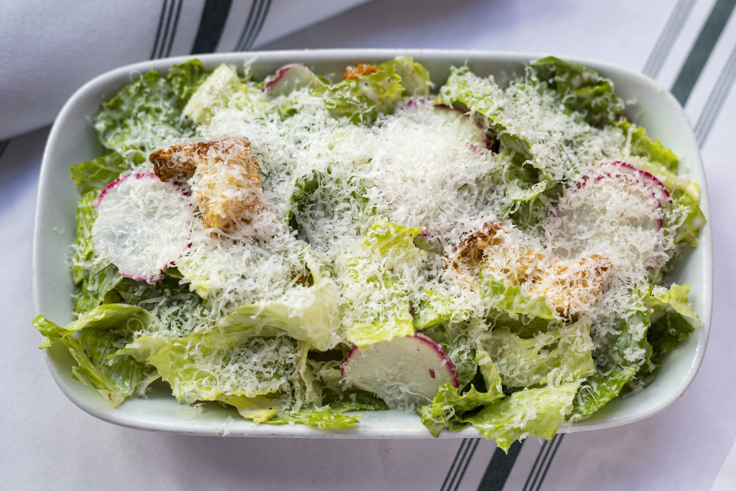 Bowl of fresh green lettuce salad topped with shredded cheese and radish slices.