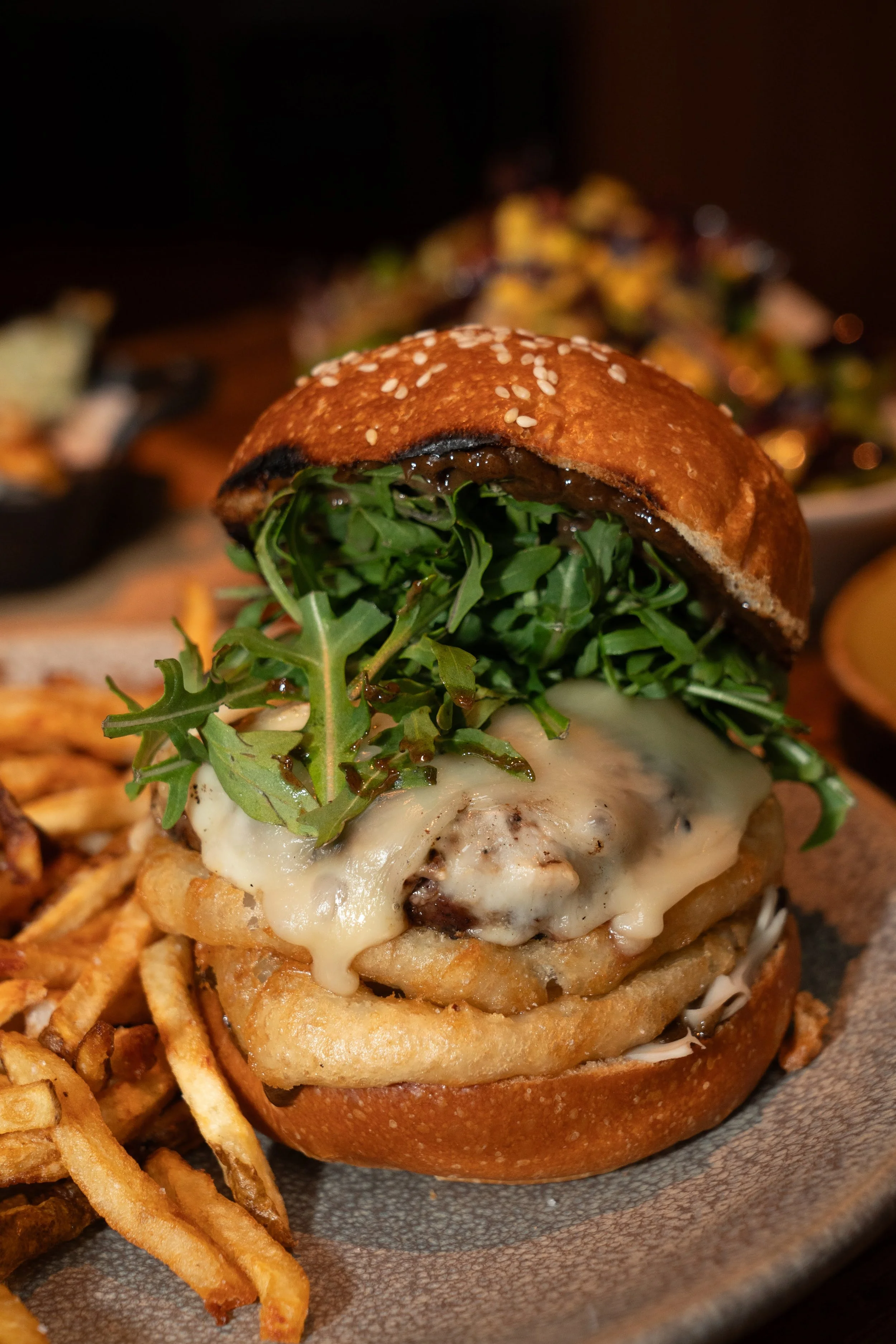 A gourmet hamburger with fresh greens, melted cheese, and a toasted bun, served on a plate with crispy fries.